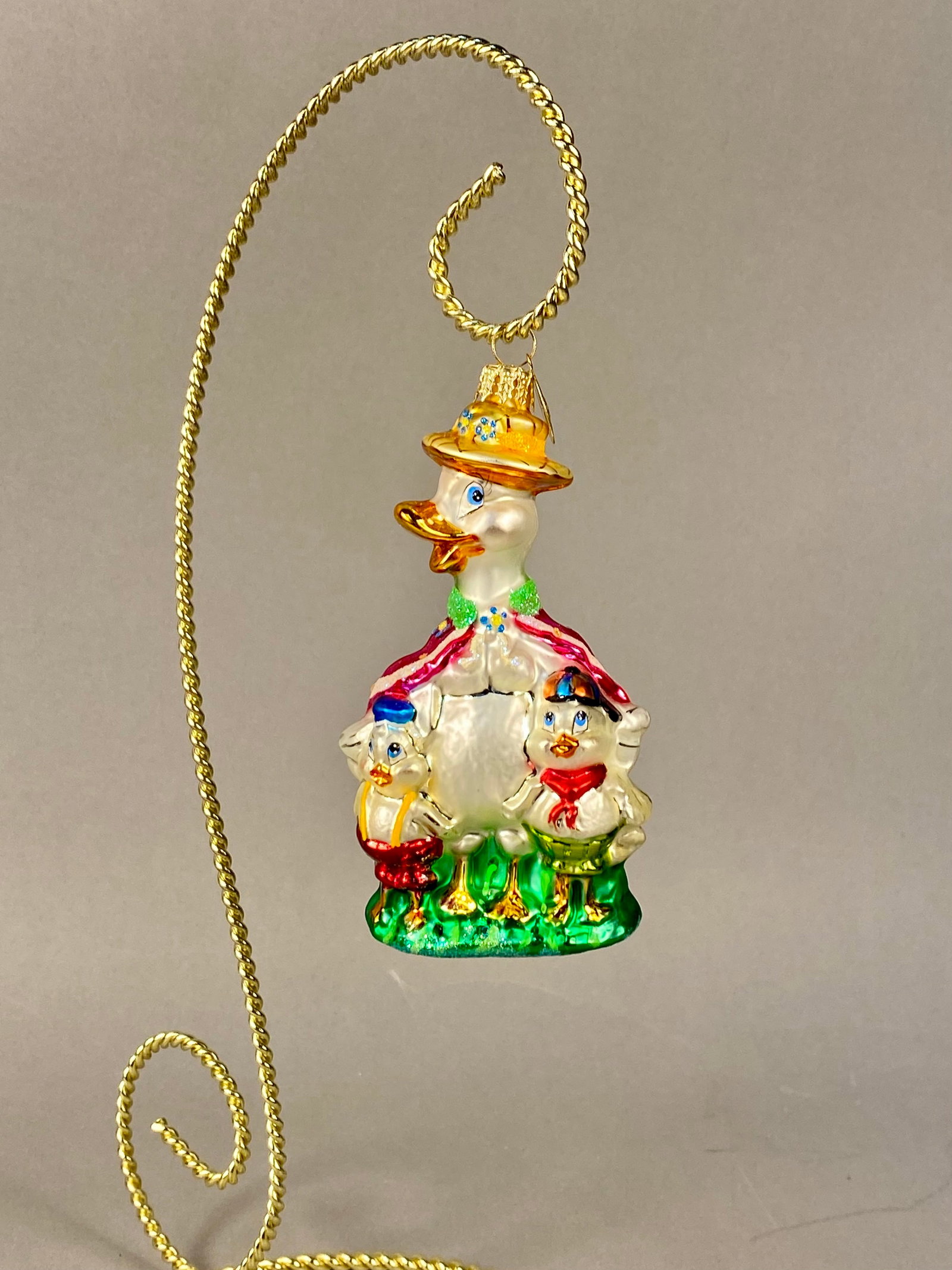 Christopher Radko Room For More Mother Duck and Ducklings Glass Ornament: A Christopher Radko hand-blown glass Christmas ornament titled Room For More. This piece features a mother duck and her two ducklings. The mother duck is decorated with a yellow sun hat featuring blue
