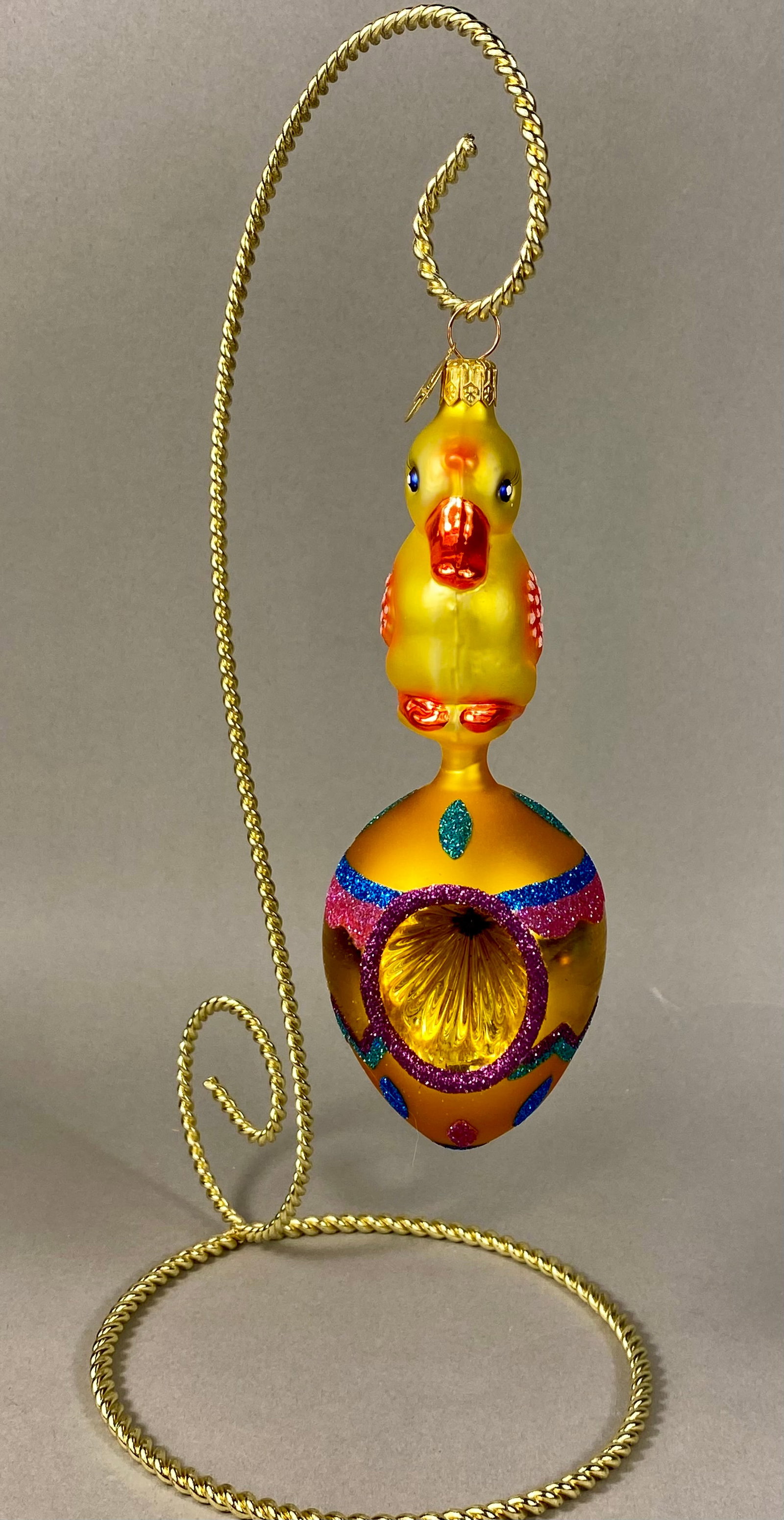 Christopher Radko Hand-Blown Glass Chick and Egg Reflector Ornament with Stand: This is a hand-blown glass figural ornament by Christopher Radko, featuring a stylized yellow chick perched atop a decorated egg. The egg base is finished in a golden yellow satin sheen and contains a