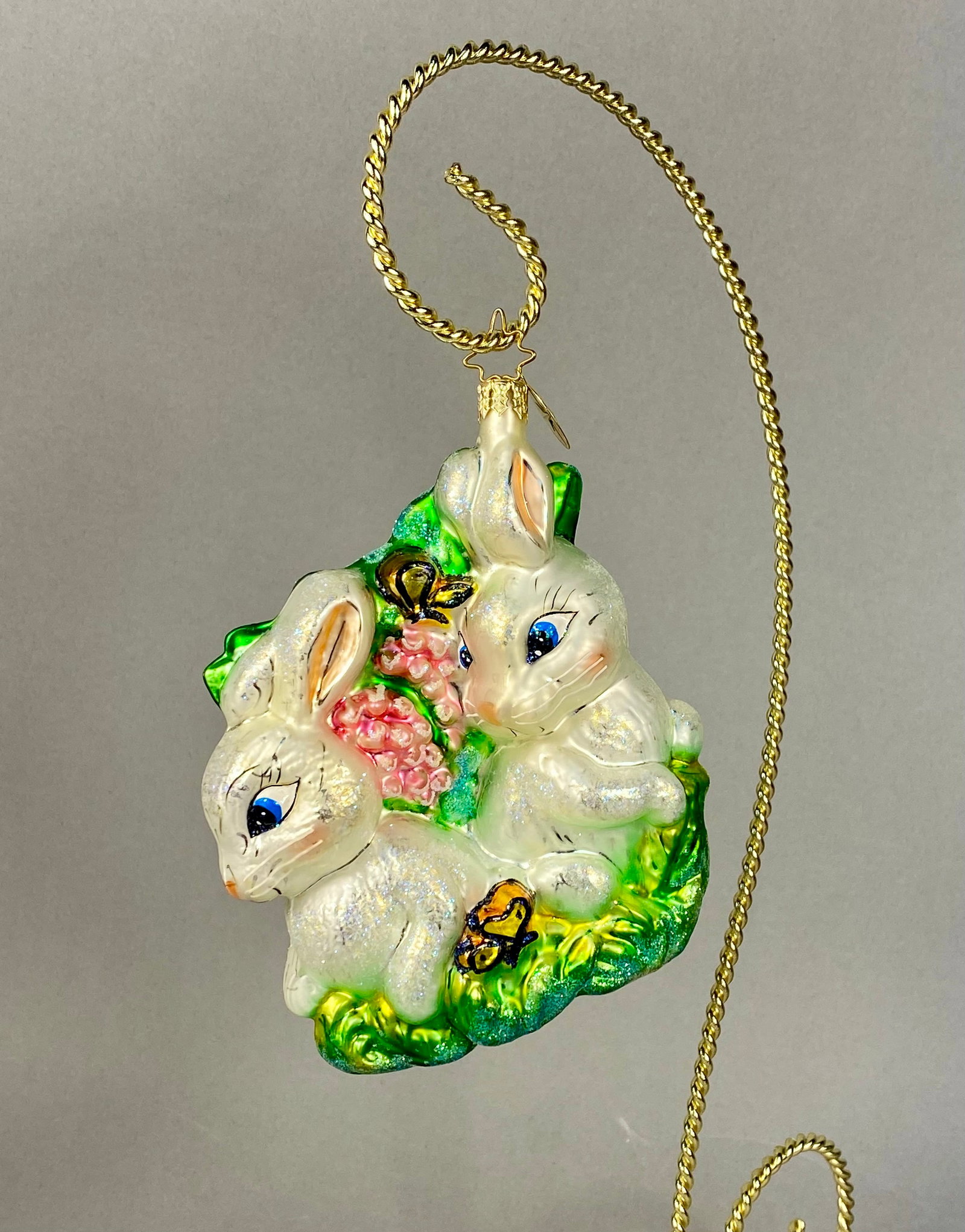 Christopher Radko Glass Bunny Rabbit Pair Christmas Ornament: Christopher Radko Hoppy Holidays mouth-blown glass Christmas ornament. The design depicts two white rabbits with iridescent glitter accents nestled in green foliage with clusters of pink flowers. The 
