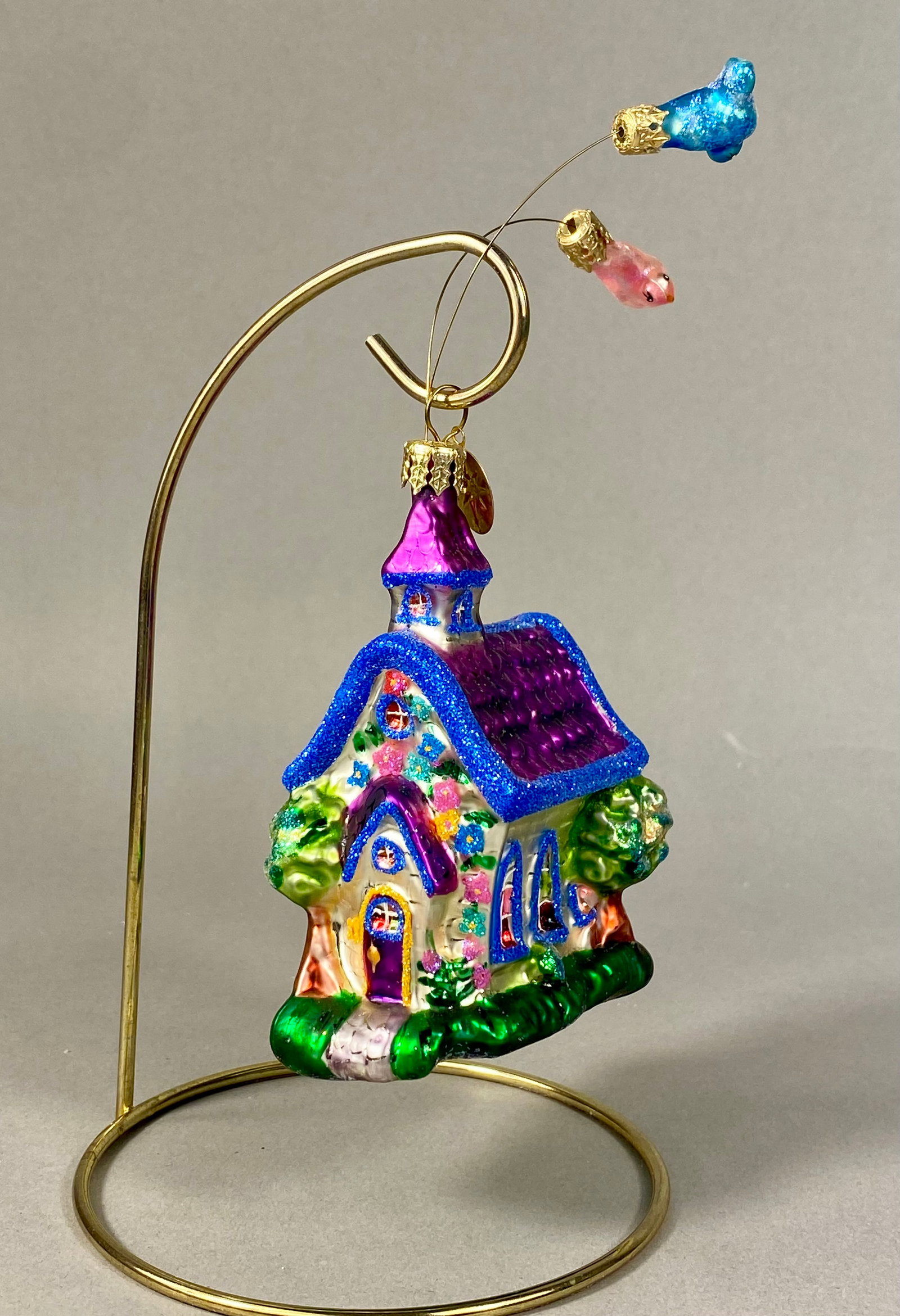 Christopher Radko Steeple Tweets Hand Blown Glass Church Ornament: A hand-blown glass Christmas ornament by Christopher Radko, identified as the Steeple Tweets pattern. The ornament depicts a chapel with white clapboard-style walls decorated with hand-painted pink an