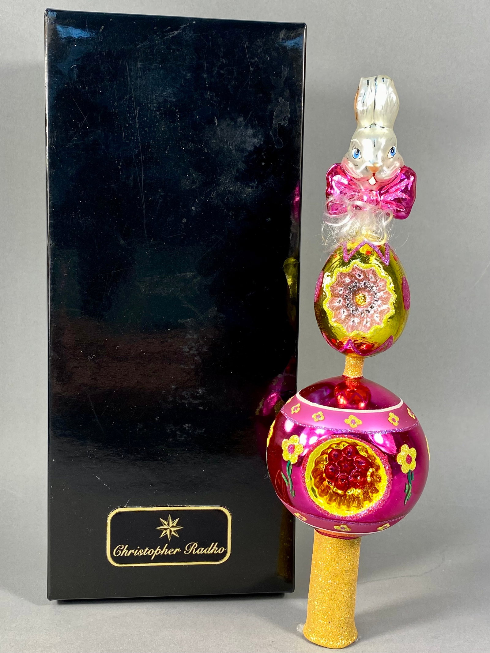 Christopher Radko Beau Bunny Hand-Blown Glass Tree Topper Finial: This is a hand-blown glass holiday tree topper, identified as the Beau Bunny Finial produced by Christopher Radko. The piece is composed of multiple stacked glass sections decorated with hand-painted 