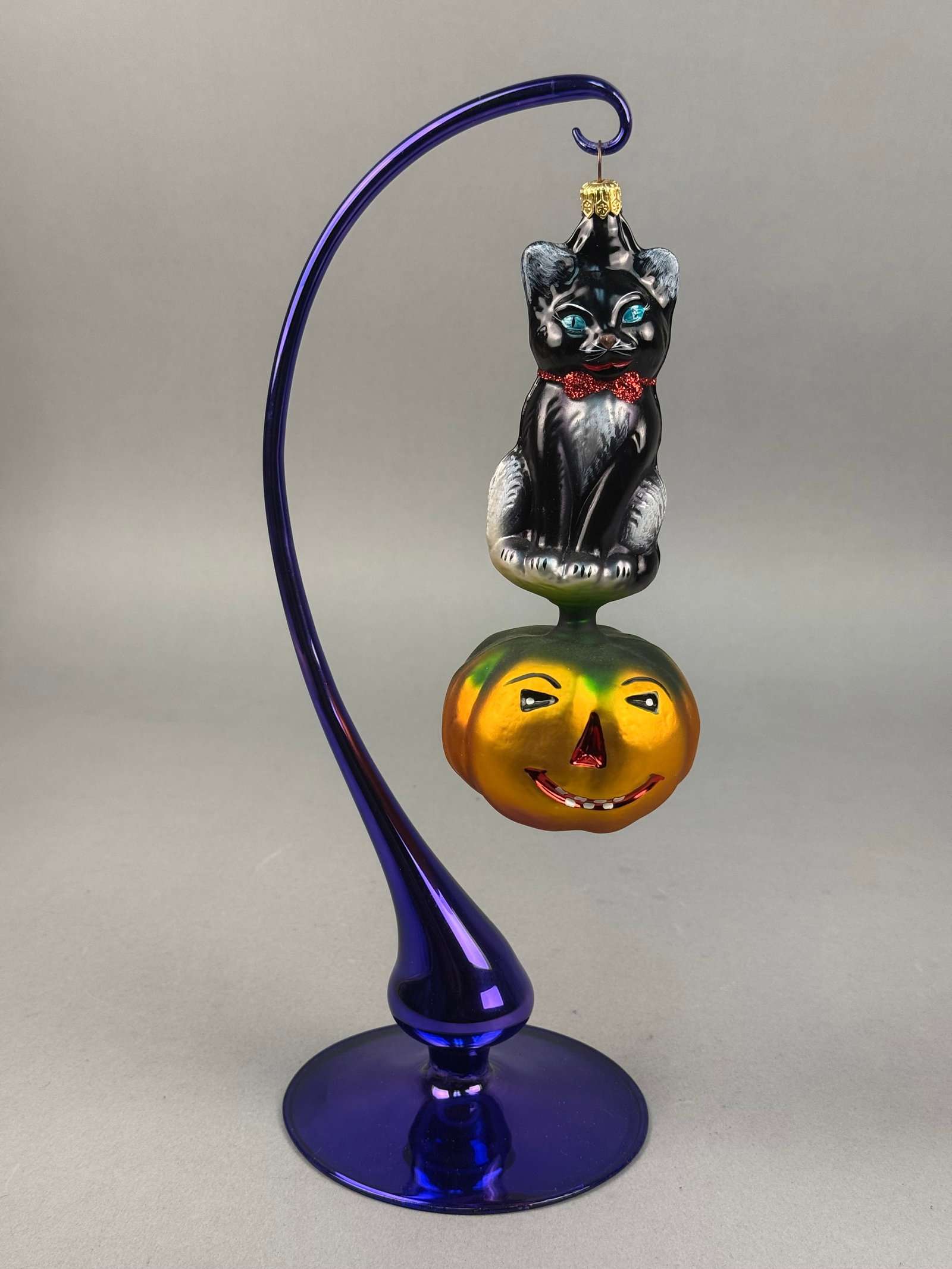 Radko Kitty Patch Black Cat and Pumpkin Glass Ornament: An art glass Halloween ornament attributed to Christopher Radko in the Kitty Patch pattern. The ornament is finished with a gold-tone fluted metal cap and a wire hanging loop adorned with a black shee