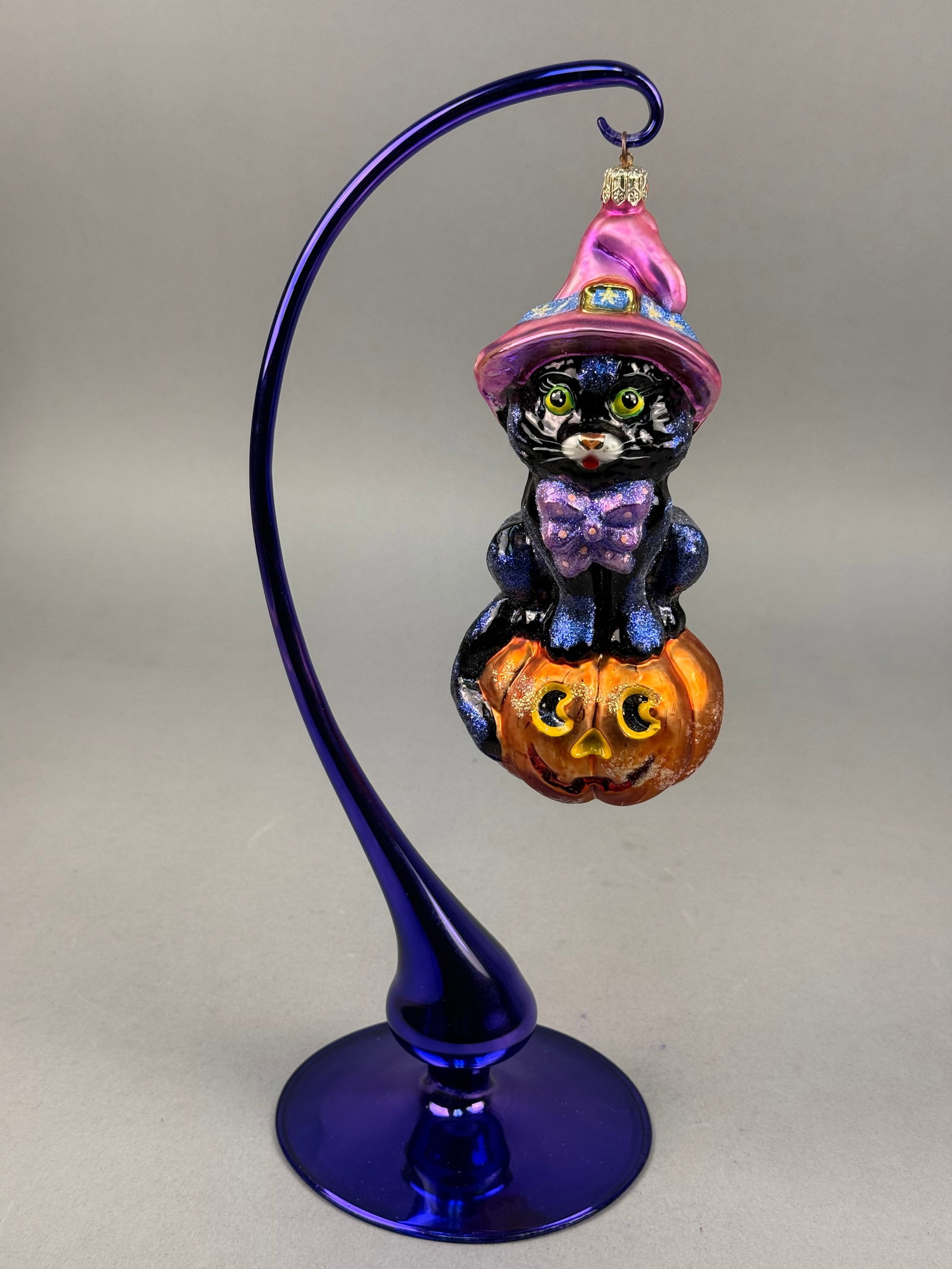 Radko Spellbound Halloween Black Cat and Pumpkin Glass Ornament: This hand-blown glass ornament, titled Spellbound by Christopher Radko, depicts a black cat in a Halloween theme. A gold-toned metal charm with an embossed eight-pointed star, the signature mark of Ch