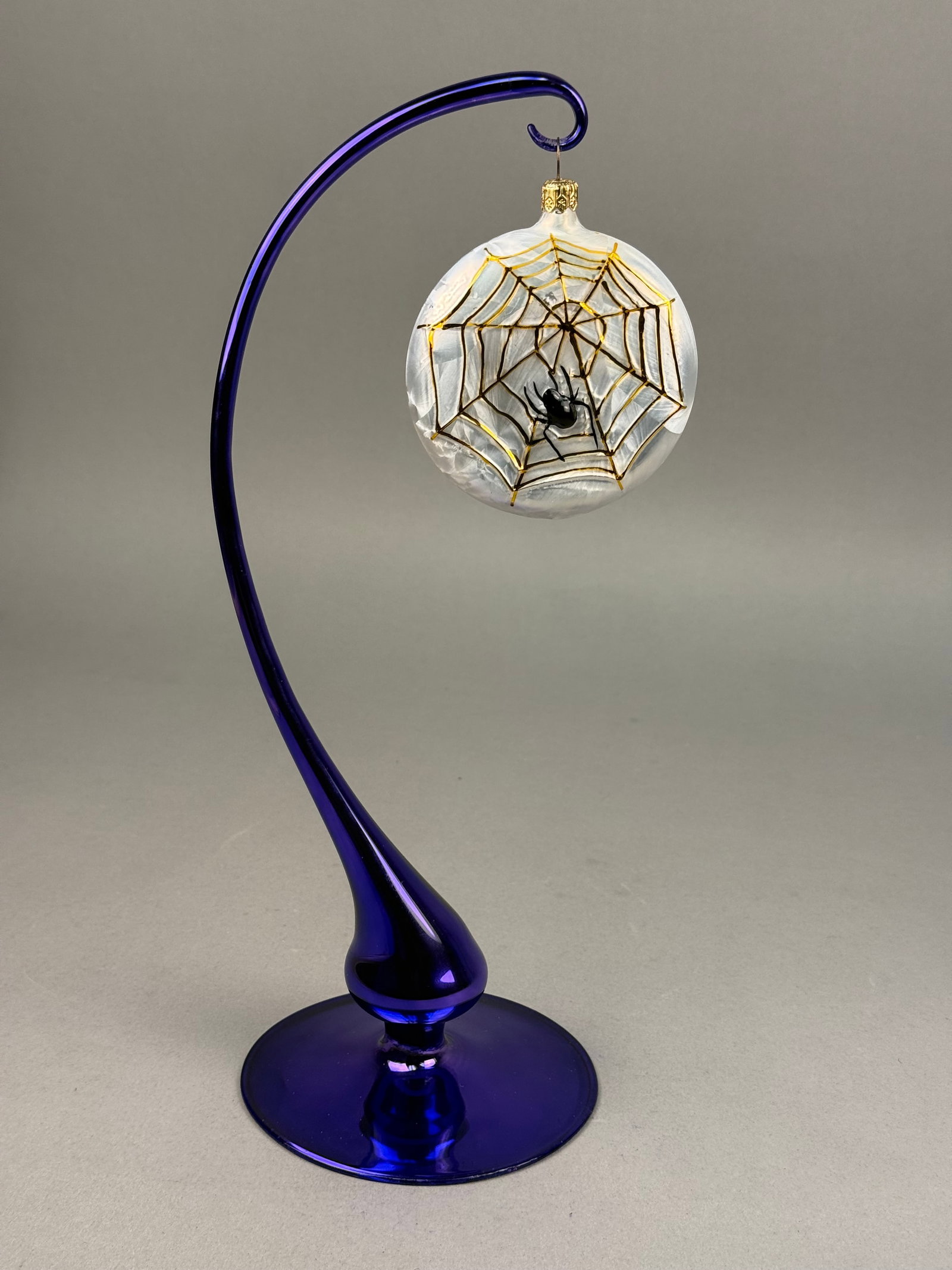 Radko Blown Glass Spiderweb Halloween Ornament: Christopher Radko disc-form blown glass ornament featuring an iridescent white interior with a feathered or striated texture. The piece is finished with a gold-tone fluted metal hanging cap. Ornament 