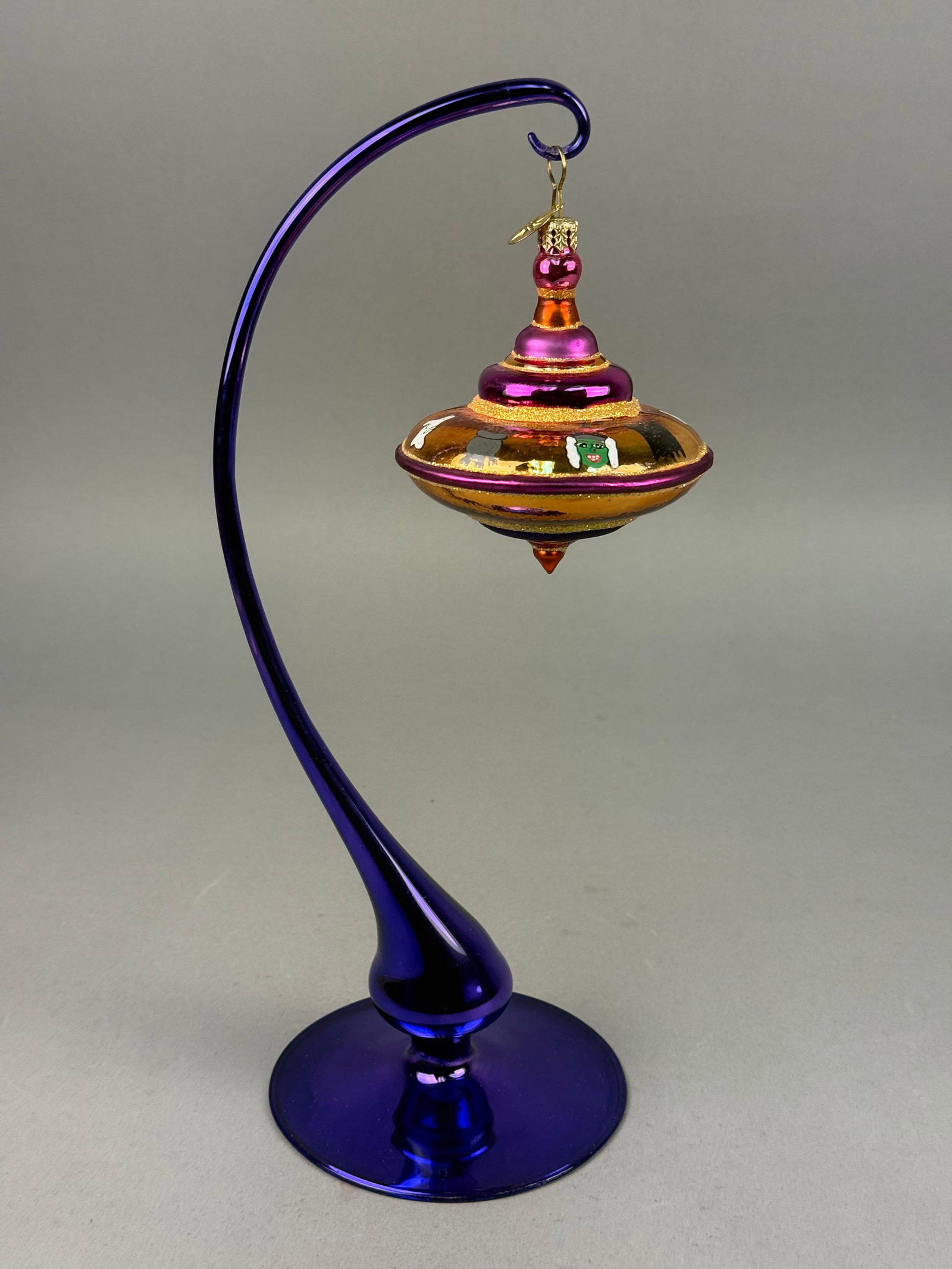 Radko Halloween Hand-Blown Glass Ornament: A hand-blown glass ornament by Christopher Radko, designed in a tiered spinning top form with a Halloween theme. The central band features a metallic gold-orange finish with hand-painted depictions of