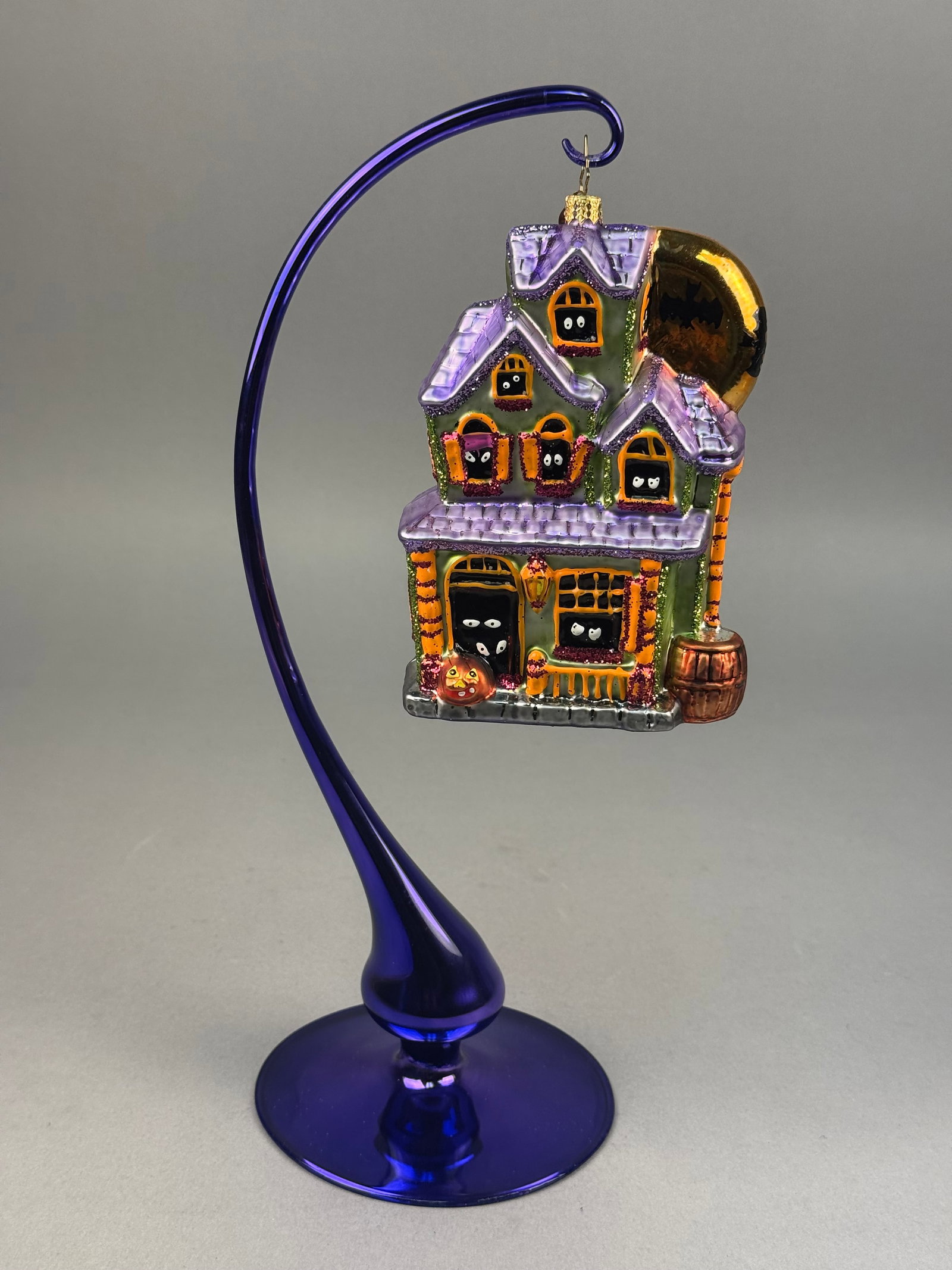 Radko Glass Haunted House Halloween Ornament: A mouth-blown glass holiday ornament by Christopher Radko, featuring a multi-gabled Victorian-style haunted house design. The ornament is fitted with a gold-toned crown-style metal cap and includes a 