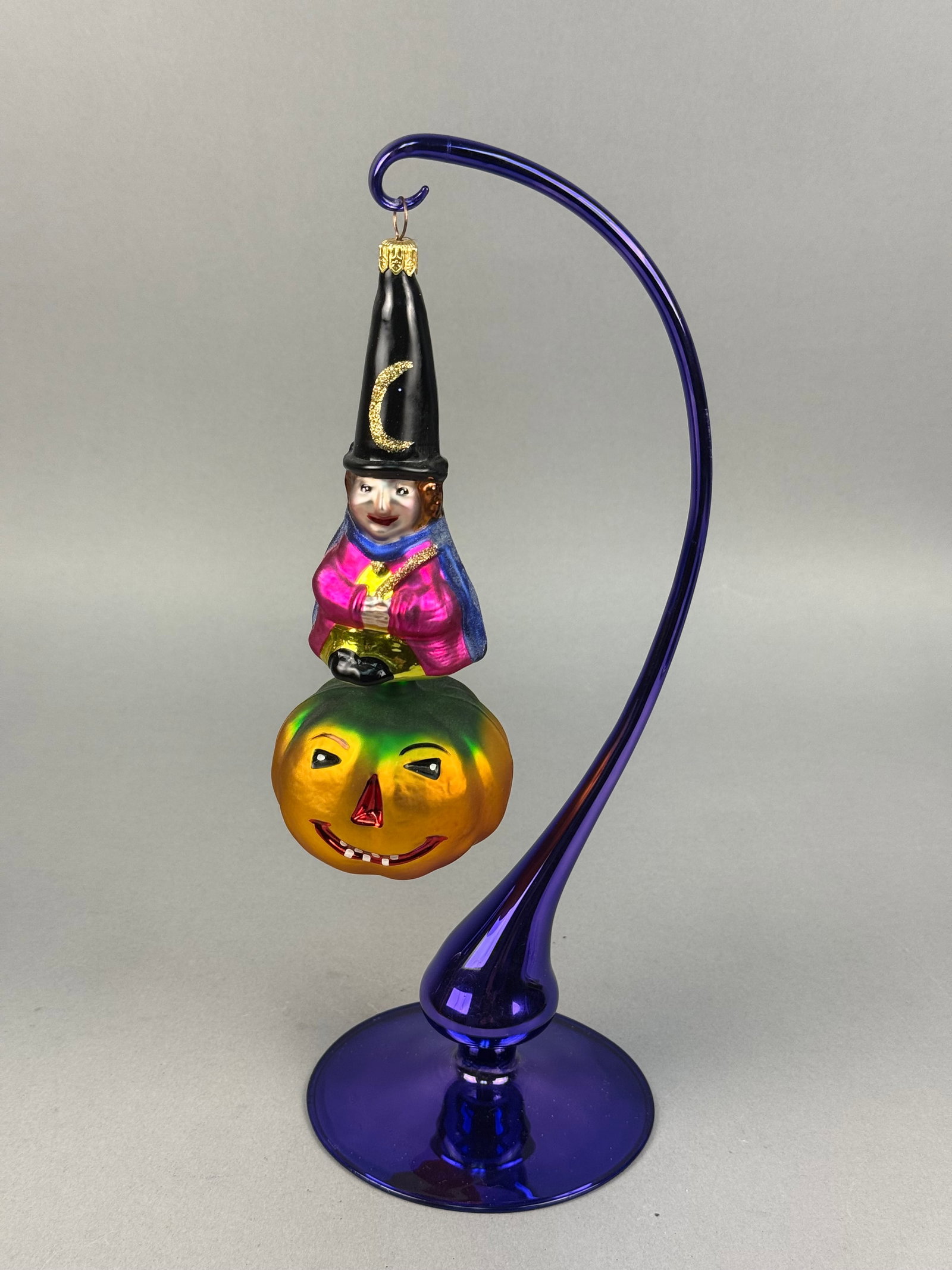 Radko Blown Glass Wizard and Pumpkin Ornament: A hand-blown glass figural ornament by Christopher Radko, depicting a wizard or witch holding a large jack-o-lantern pumpkin. It is suspended from a gold-tone metal cap stamped with RADKO. Ornament st