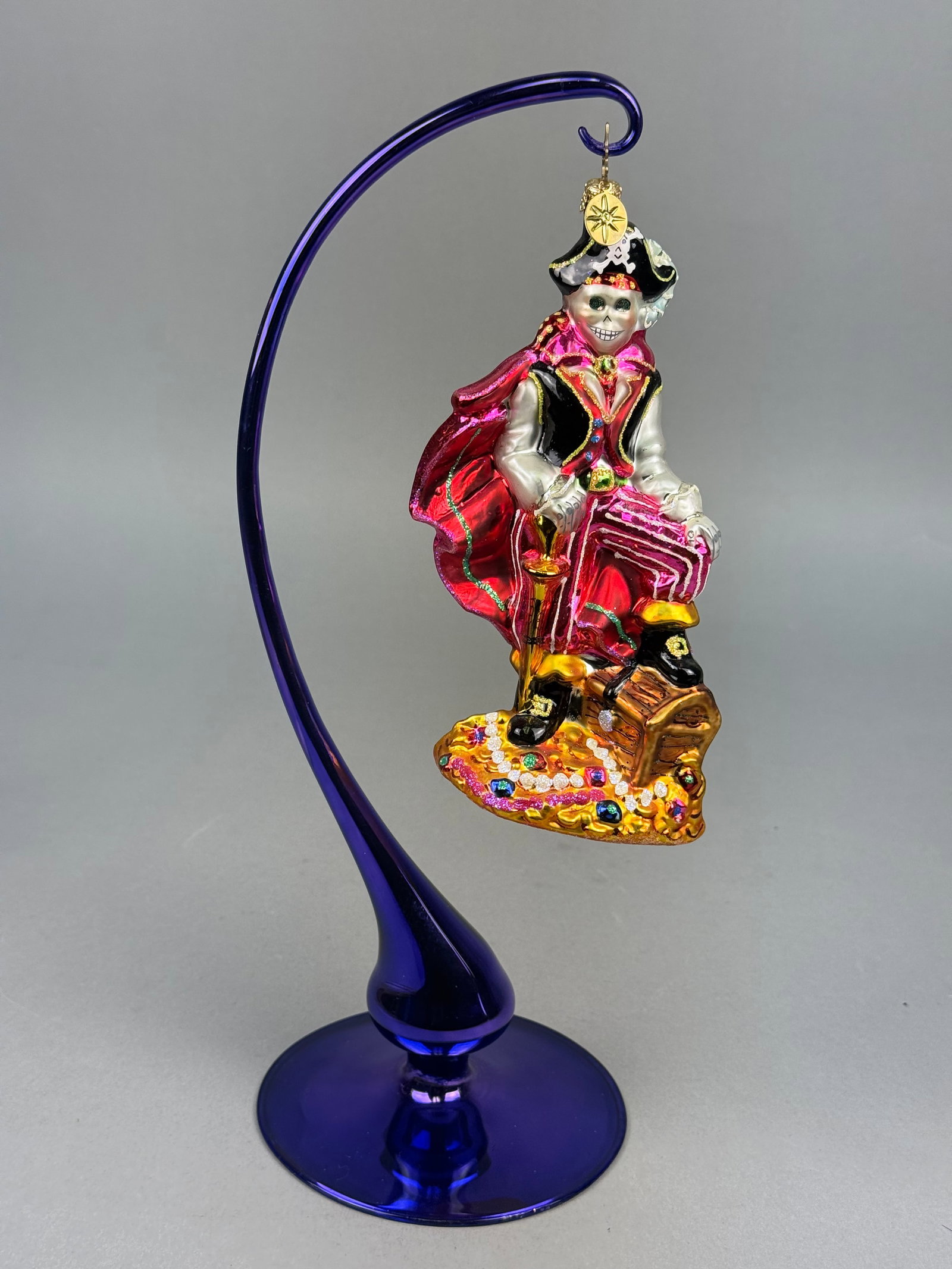Radko Blown Glass Skeleton Pirate Ornament: Hand-blown glass holiday ornament featuring a skeleton pirate in the style of Dia de los Muertos iconography. The figure is depicted with a wide grin and large eye sockets, wearing a black tricorne ha