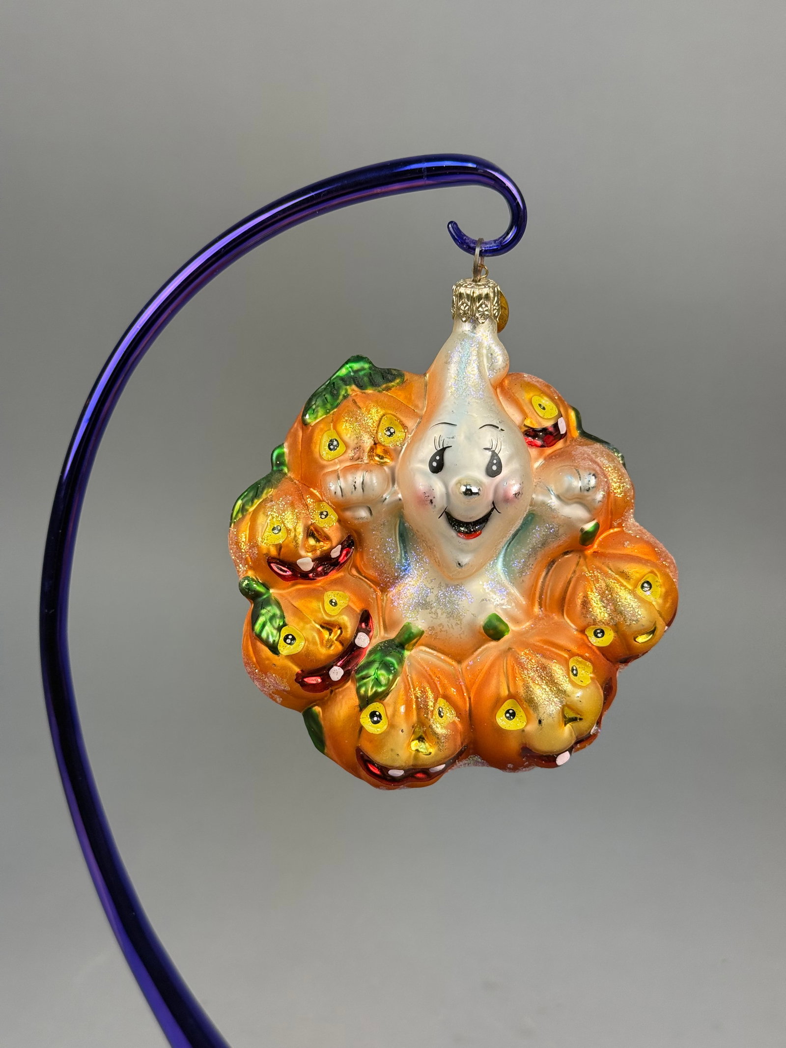 Radko Giggles and Boo Glass Halloween Ornament: A Christopher Radko hand-blown glass Halloween ornament titled Giggles and Boo. The piece features a central smiling white ghost figure with rosy cheeks and iridescent glitter accents, encircled by a 