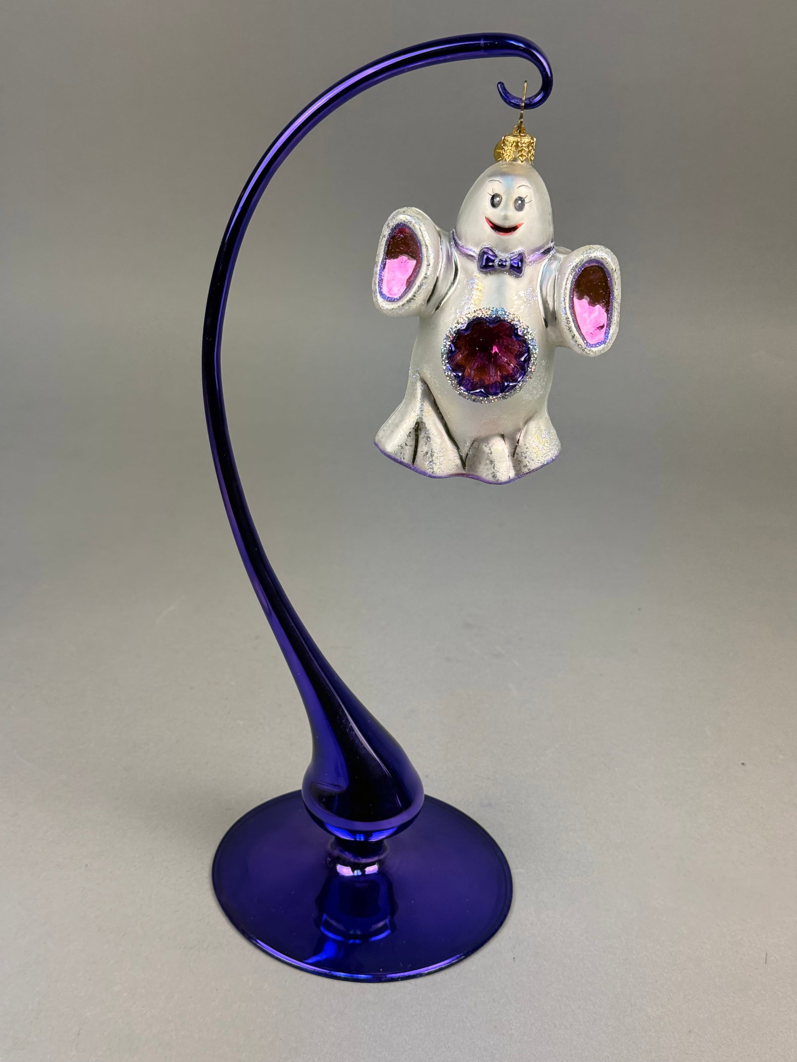 Radko Blown Glass Ghost Ornament: A hand-blown glass holiday ornament manufactured by Christopher Radko. The piece is a ghost figure featuring a pearlescent white finish and multicolored glitter accents throughout the body. Identifica