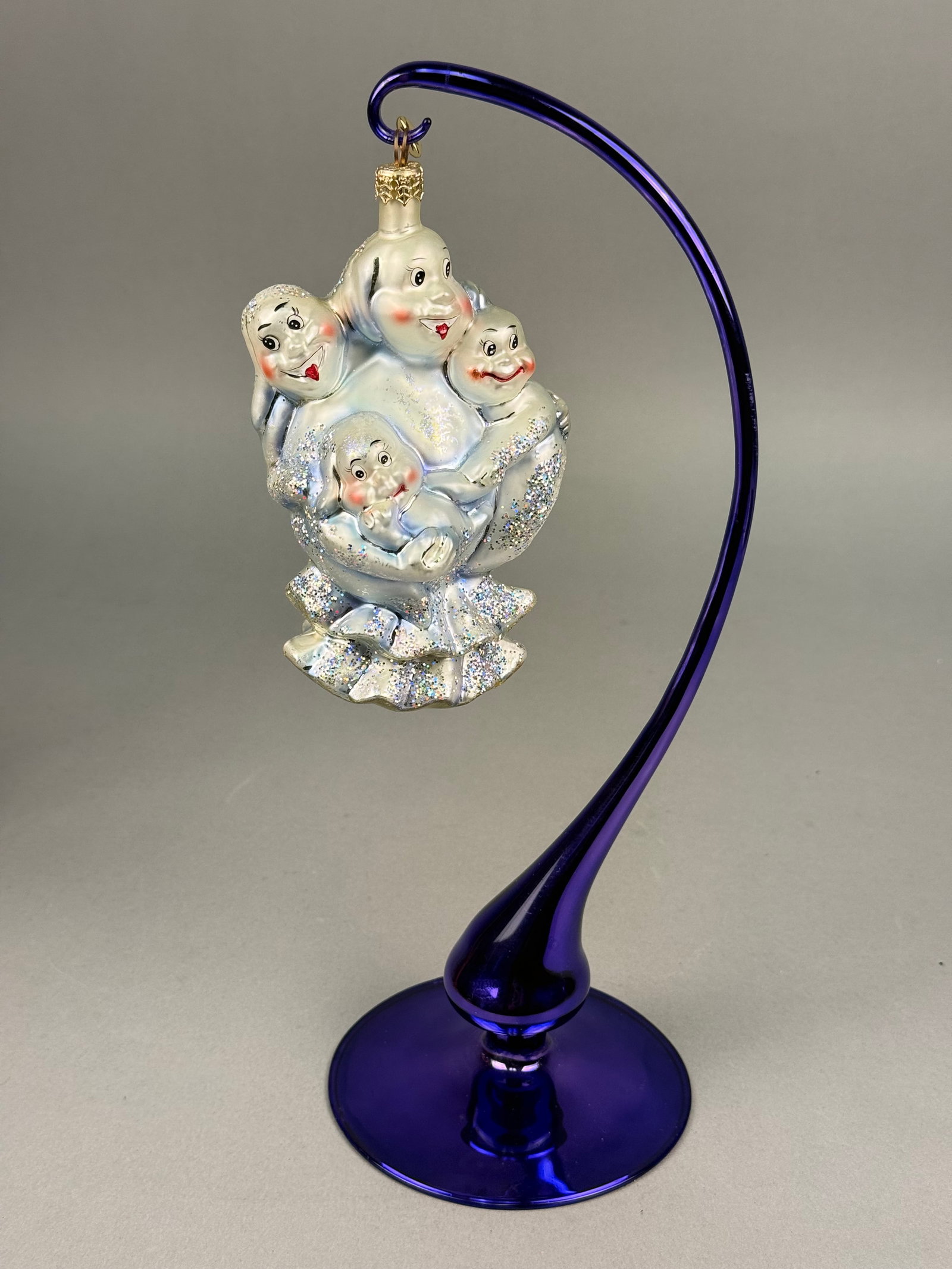 Radko Blown Glass Ghosts Ornament: This mouth-blown glass Christmas ornament is attributed to Christopher Radko based on the distinctive gold-toned metal starburst charm attached to the hanging loop. The ornament features a vertical ar
