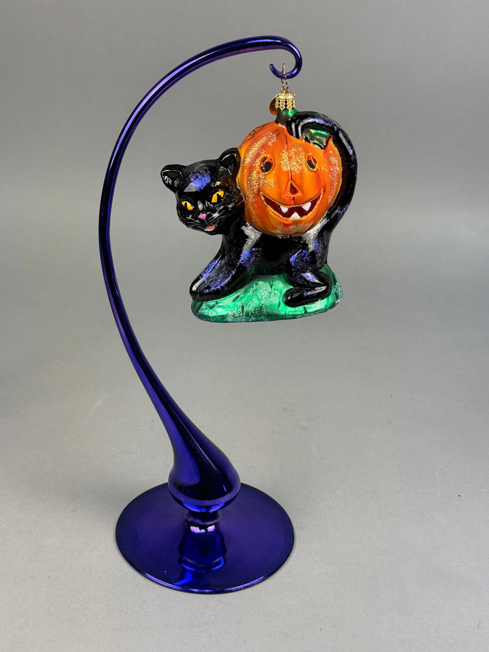Radko Halloween Black Cat and Jack-o-Lantern Glass Ornament: This is a mouth-blown glass holiday ornament from the Christopher Radko collection, featuring a Halloween-themed design. The figure depicts a black cat with purple iridescent glitter highlights posed 