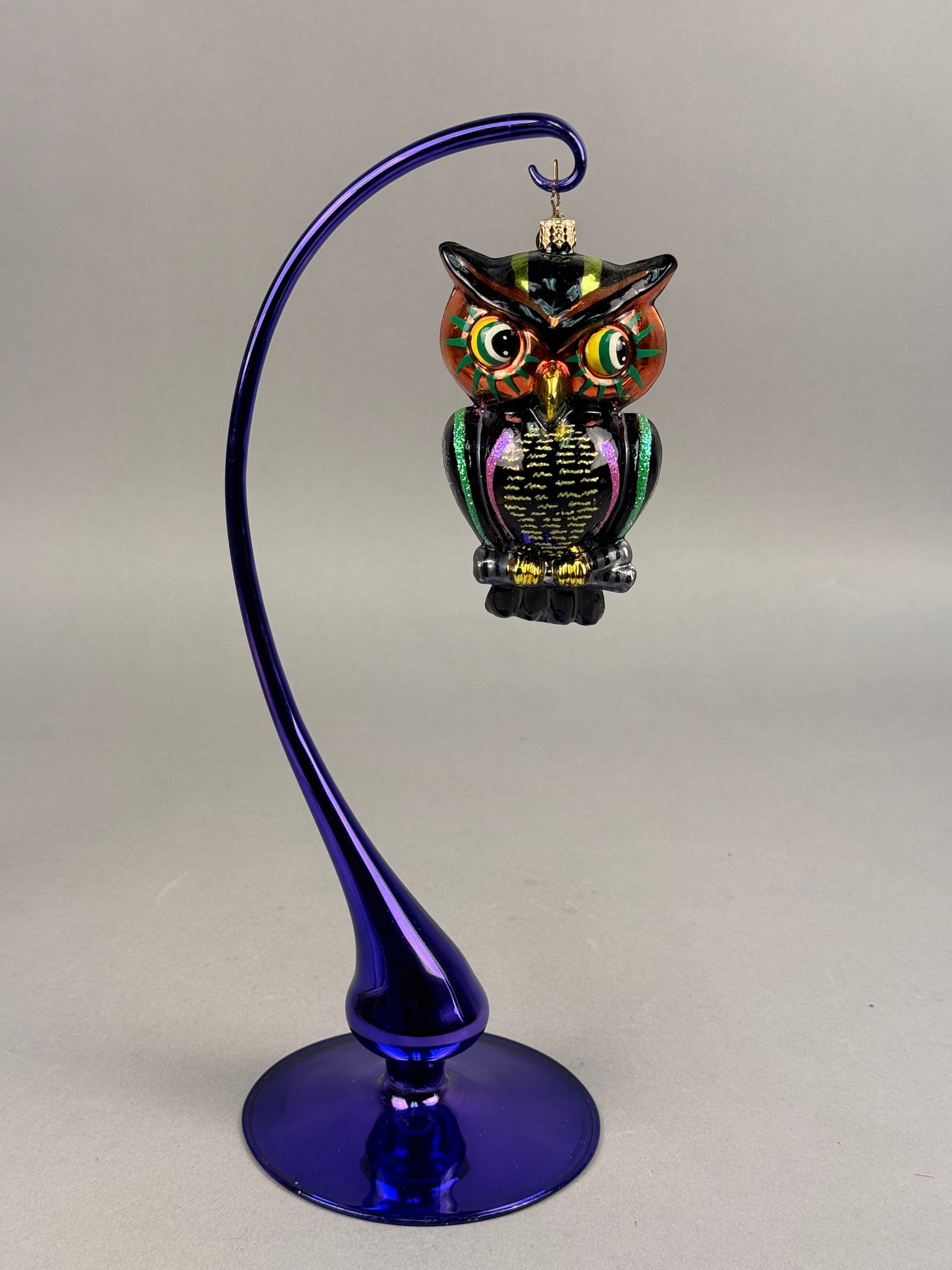 Radko Blown Glass Owl Halloween Ornament: A hand-blown glass ornament by Christopher Radko depicting a stylized owl. The ornament features a black glass body with an iridescent blue glitter finish on the reverse. The piece is fitted with a de