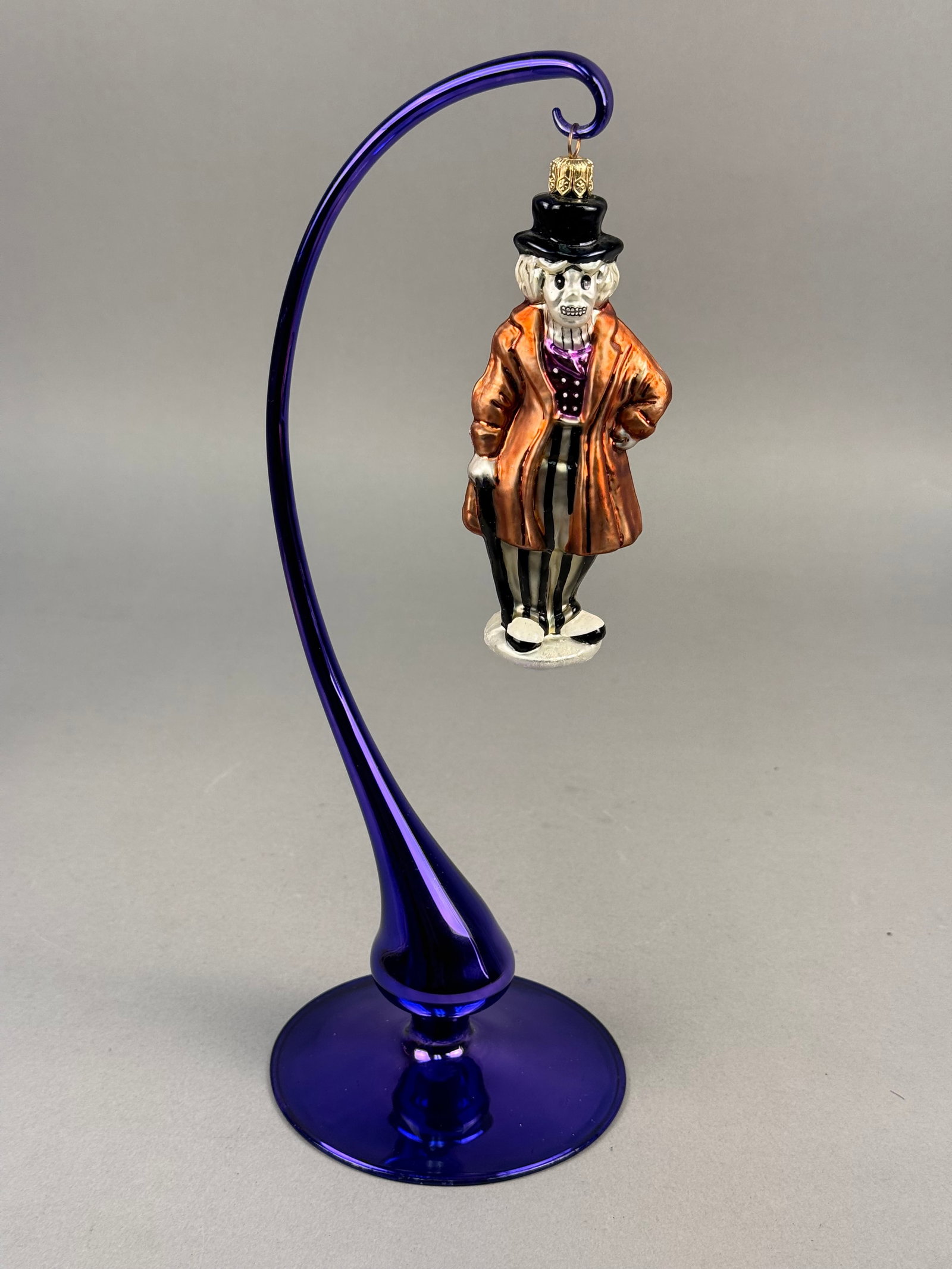 Radko Skeleton Gentleman Halloween Ornament: A glass skeleton gentleman ornament by Christopher Radko, featuring a copper-colored coat and striped trousers. Ornamnent stand NOT INCLUDED approximately 5.5 inches tall Excellent condition free from