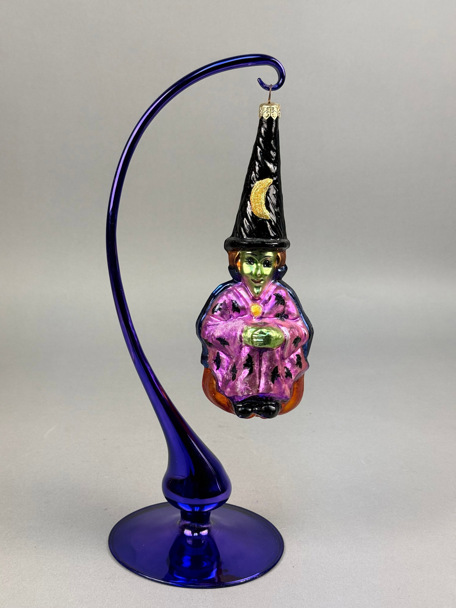 Radko Blown Glass Witch Ornament: This lot features a hand-blown glass holiday ornament by Christopher Radko depicting a whimsical witch figurine. The piece is crafted with an iridescent green face featuring hand-painted facial detail