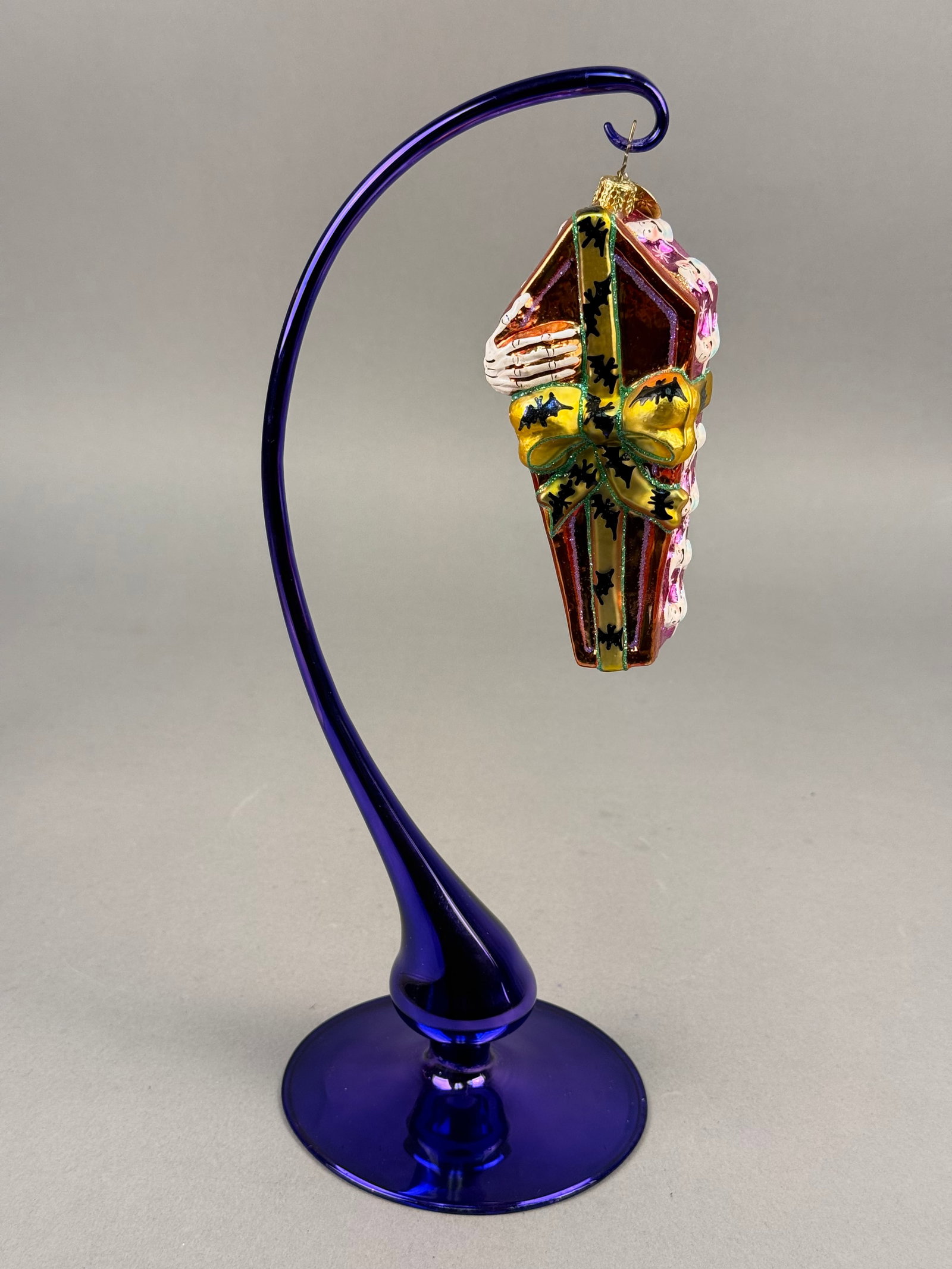 Radko Blown Glass Halloween Coffin Ornament: A hand-blown glass Halloween ornament produced by Christopher Radko in the form of a stylized coffin. The piece includes a gold-toned metal cap and hanging loop with an attached circular metal charm f