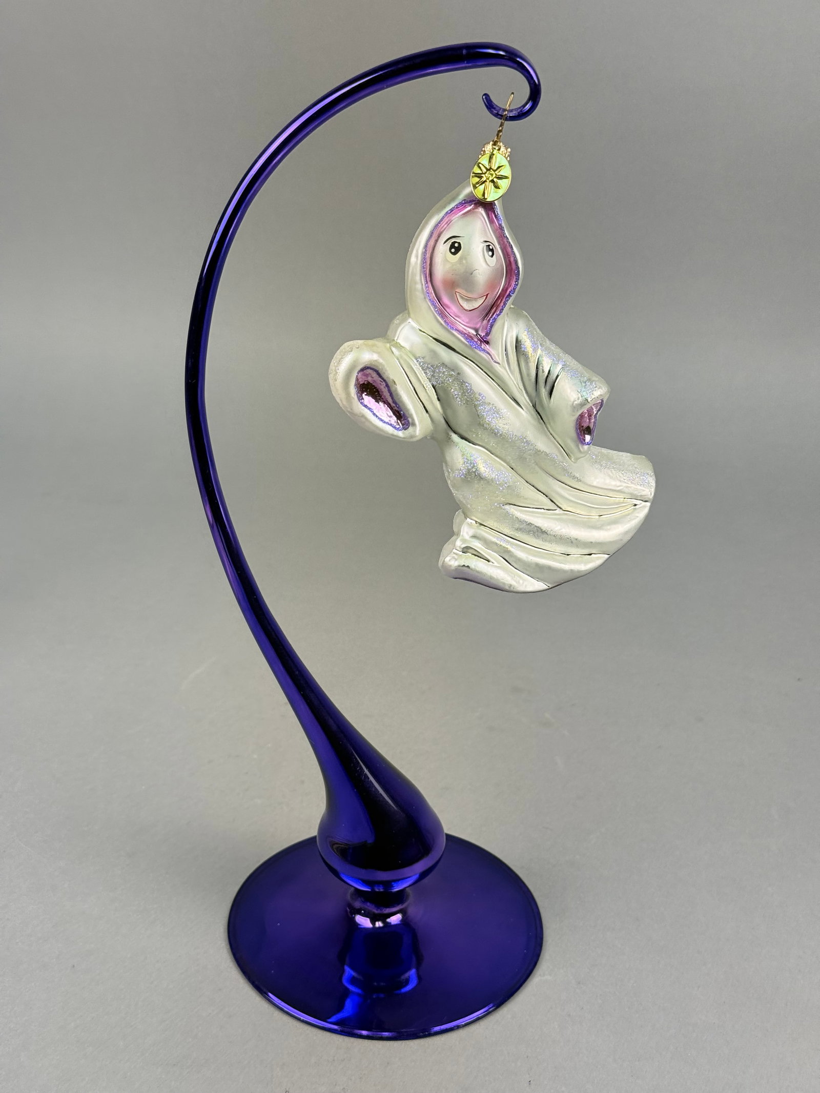 Radko Blown Glass Halloween Ghost Ornament: The ornament is mold-blown with a silvered interior and depicts a stylized hooded figure with hand-painted facial details. The piece includes a gold-toned metal cap with a star-shaped wire hanger and 