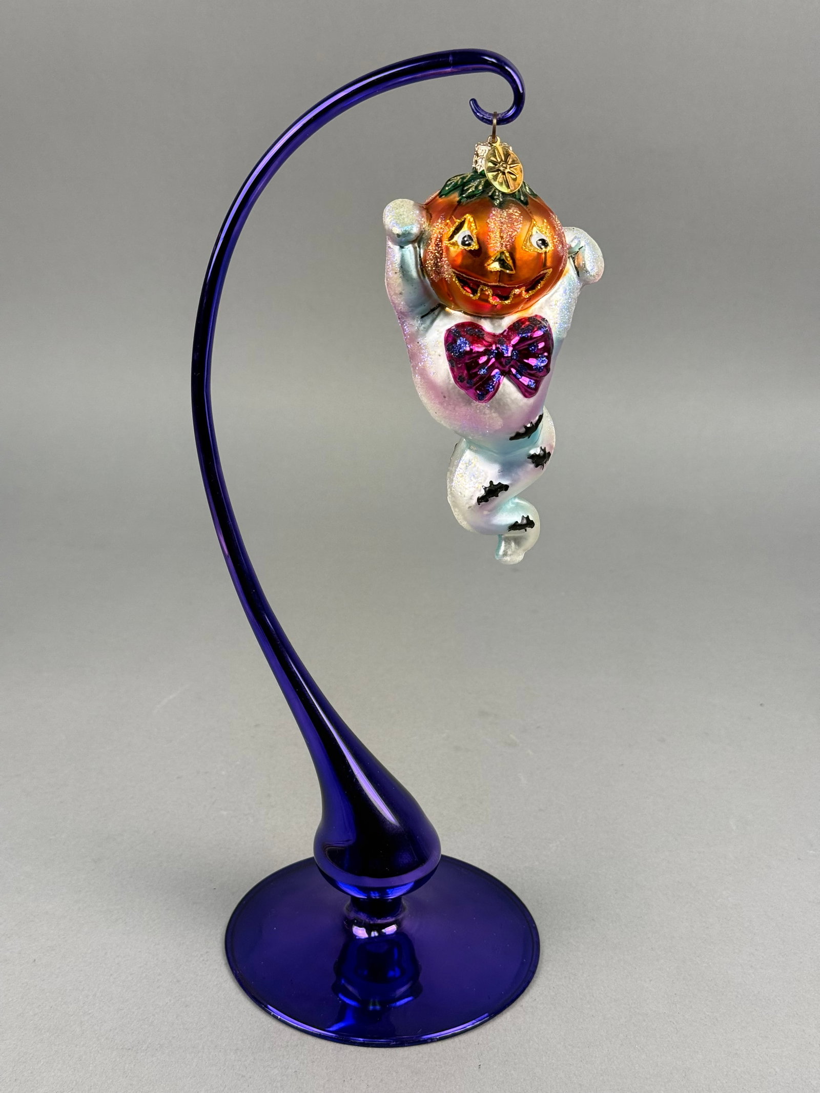 Radko Pumpkin-Headed Ghost Glass Ornament: This hand-blown glass ornament, produced by Christopher Radko, features a whimsical Halloween figure that combines a jack-o'-lantern and a ghost. The piece is constructed from glass with a silvered in