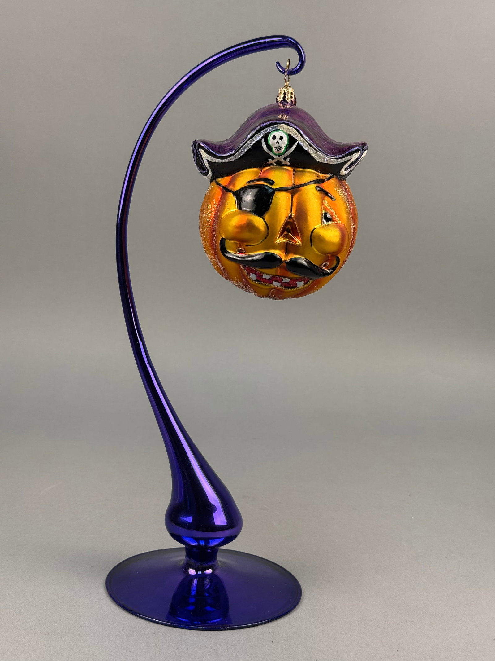 Radko Blown Glass Pirate Pumpkin Ornament: A hand-blown glass holiday ornament produced by Christopher Radko, featuring a whimsical pirate-themed jack-o-lantern design. The ornament features the signature gold-toned metal charm embossed with a