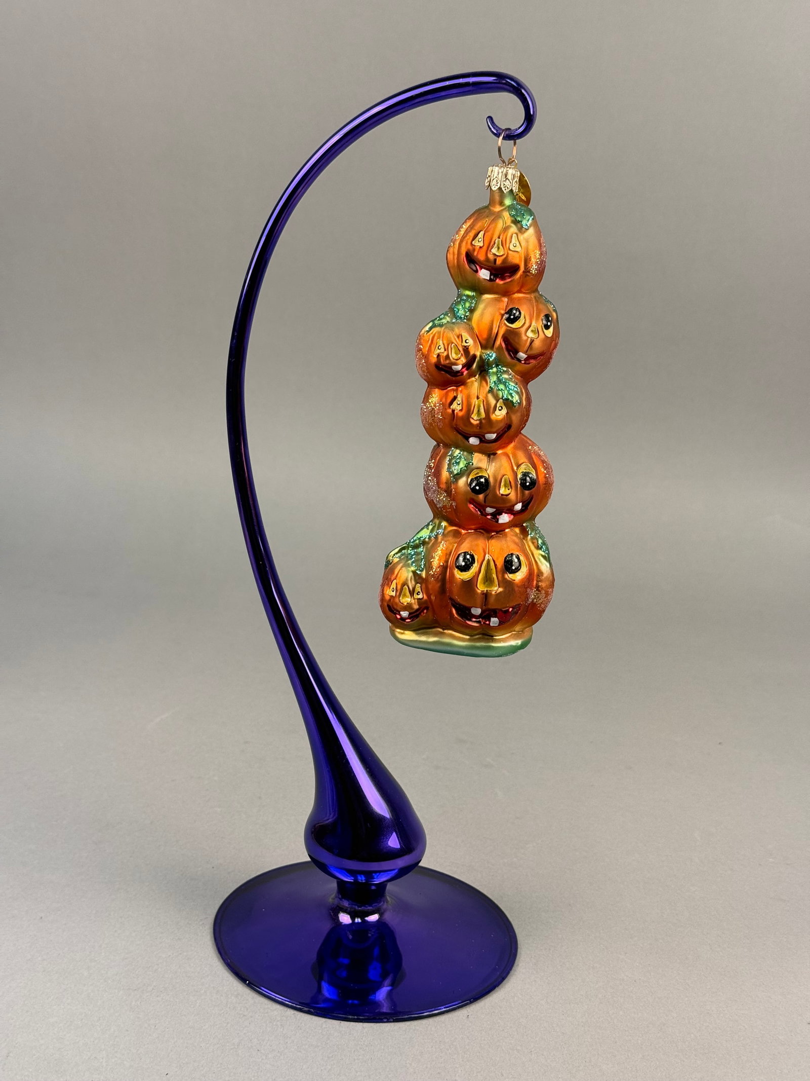 Radko Blown Glass Halloween Stacked Jack-o-lantern Ornament: This hand-blown glass ornament by Christopher Radko features a vertical stack of five interconnected jack-o-lantern pumpkins. ed gold and orange glitter. The base of the lowest pumpkin is finished in 