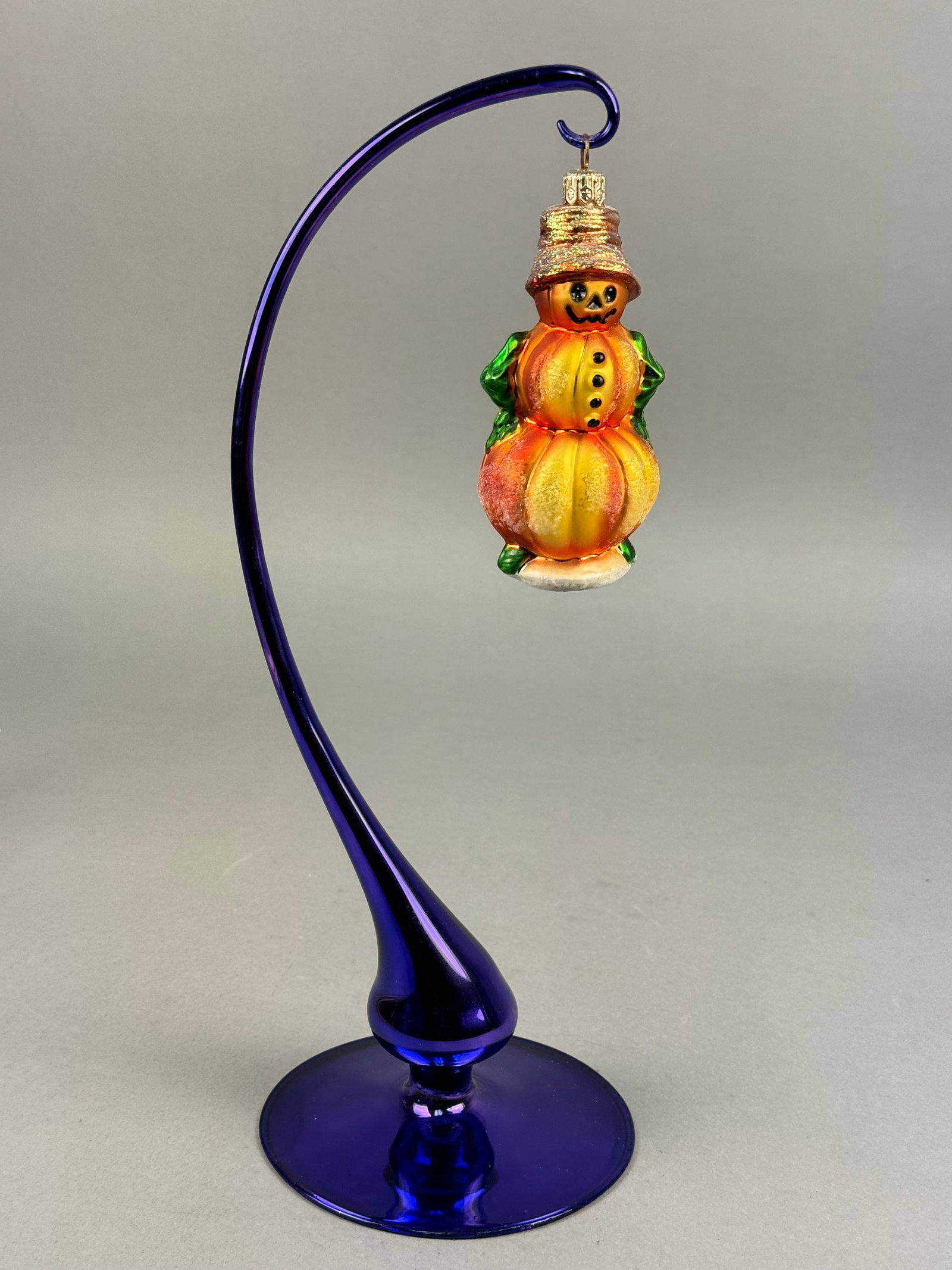 Radko Pumpkin Snowman Hand-Blown Glass Ornament: A hand-blown glass holiday ornament by Christopher Radko. The ornament is shaped as a figure composed of three graduated, stacked pumpkins. T The ornament features an orange and yellow gradient finish