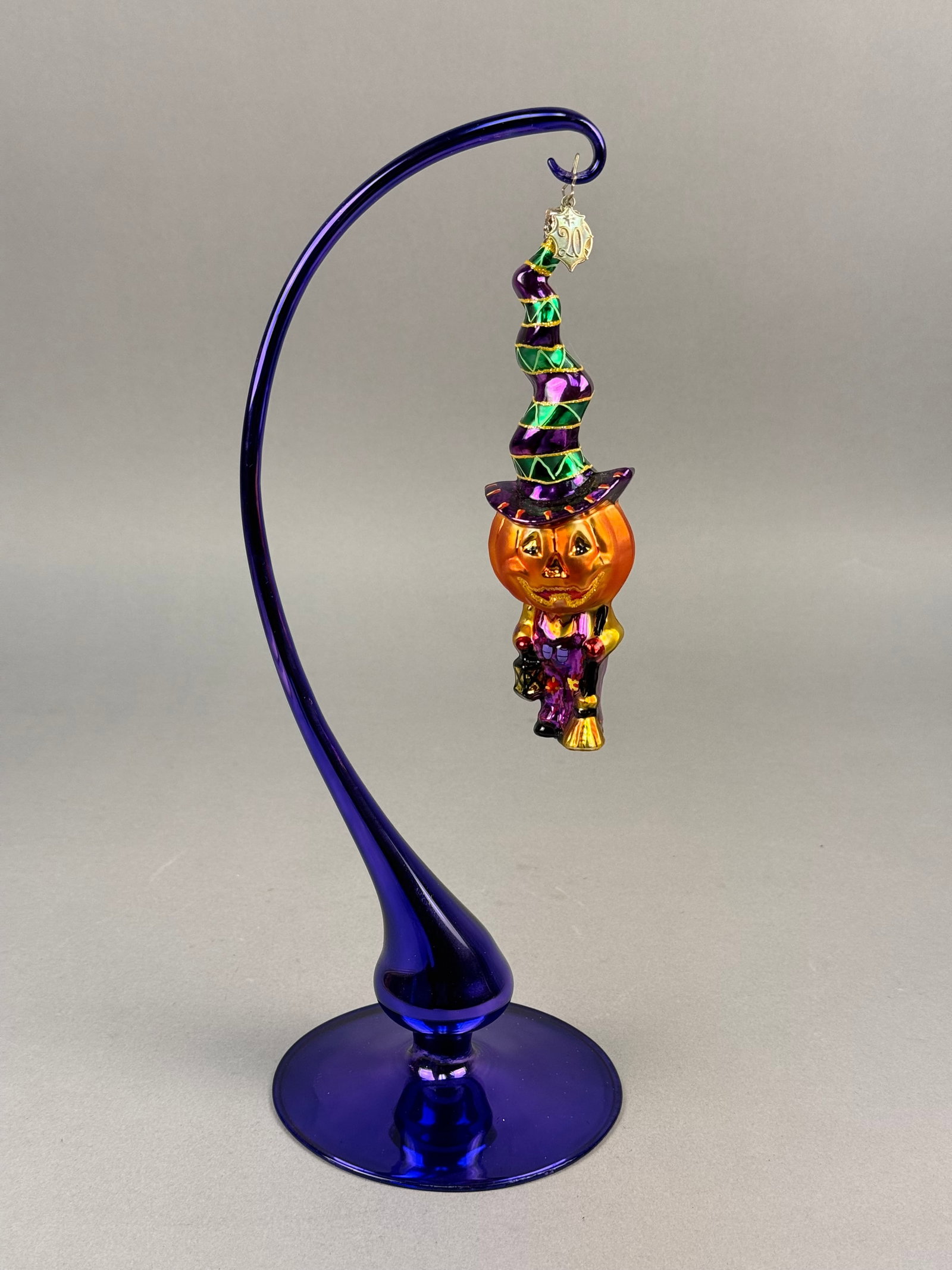 Radko Hand-Blown Glass Halloween Ornament: A hand-blown glass Halloween ornament designed by Christopher Radko, featuring a flying jack-o'-lantern character. The ornament is fitted with a silver-toned metal crown-style cap at the top of the ha