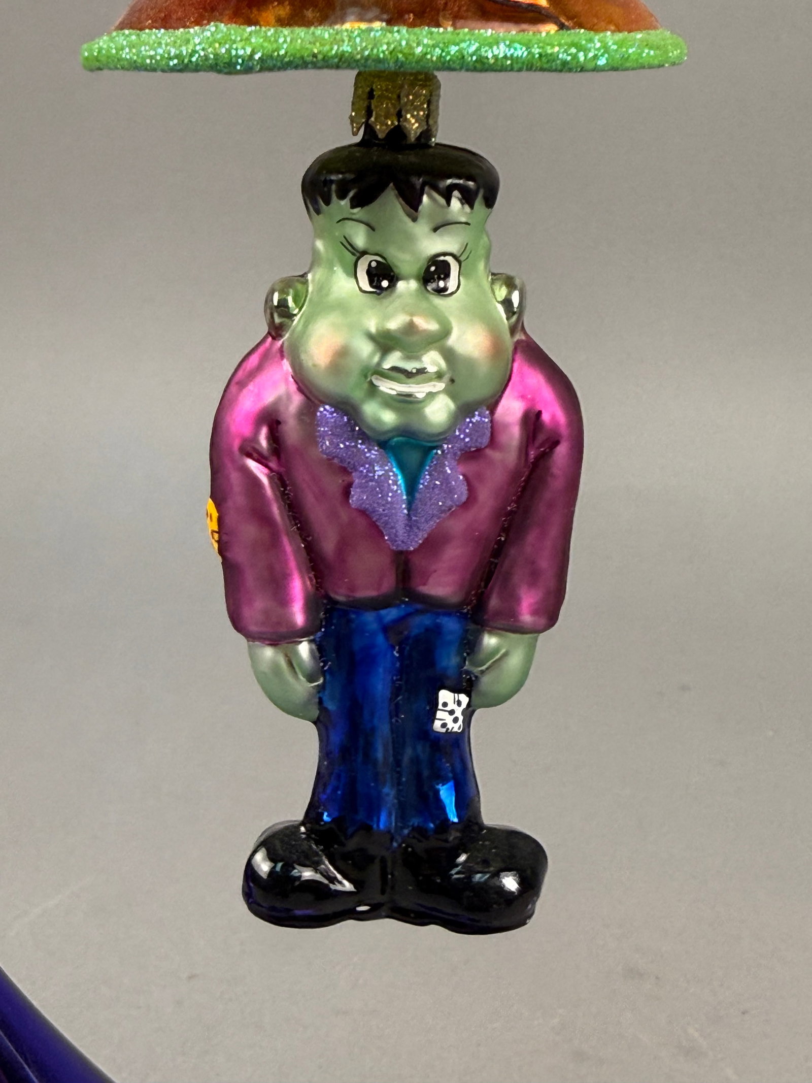 Christopher Radko Frankenstein and Halloween Bell Glass Ornament: This hand-blown glass Halloween ornament is by Christopher Radko. The piece features a double-sided design. One side represents Frankensteinâ€™s monster with a green face, black hair, a purple