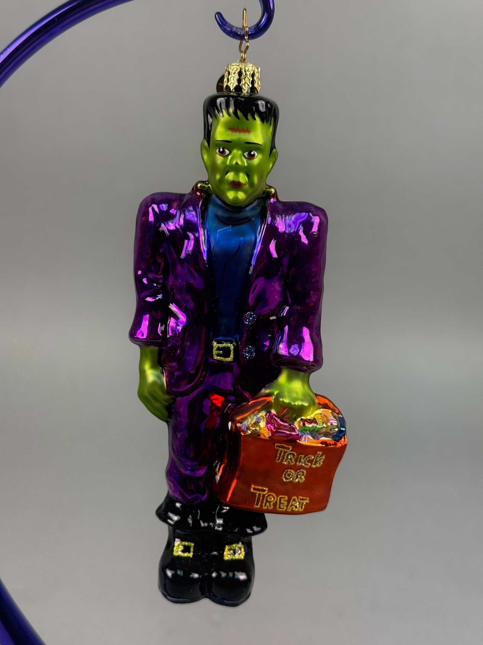 Christopher Radko Frankenstein Trick or Treat Glass Halloween Ornament: A mouth-blown and hand-painted glass holiday ornament depicting Frankenstein's monster in a Halloween theme. The figure is rendered with a lime green complexion, a red stitched scar on the forehead, a
