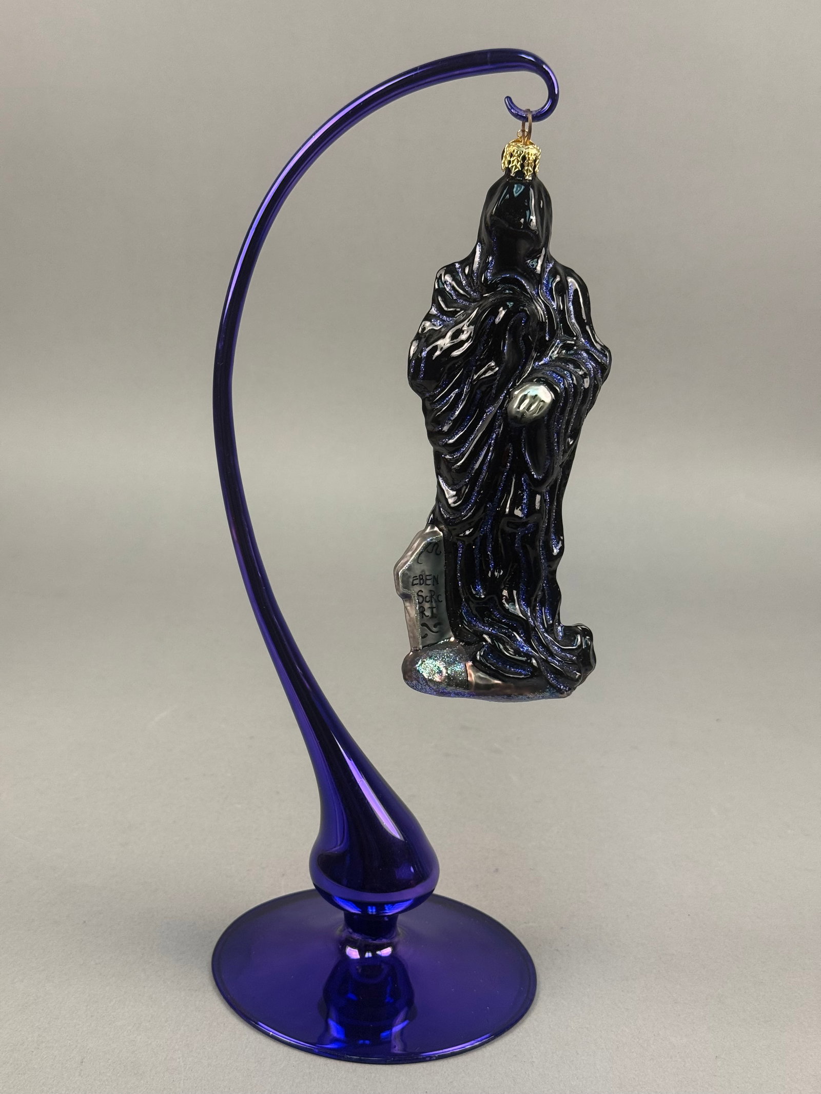 Eben Horton Hand-Sculpted Glass Ghost of Christmas Yet to Come Ornament on Stand: A hand-sculpted glass figural ornament by artist Eben Horton, depicting the Ghost of Christmas Yet to Come. The figure is rendered in a deep black glass with a heavily textured surface featuring flowi