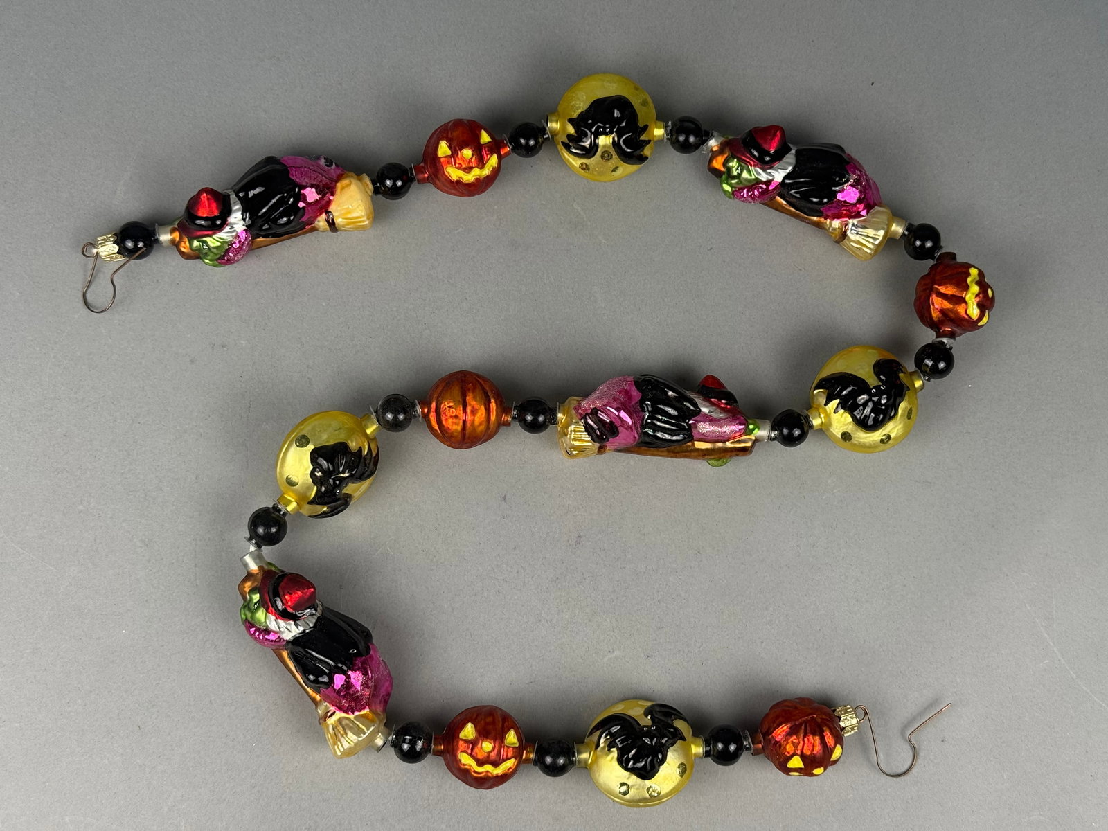 Radko Hand-Blown Glass Halloween Garland: A Halloween-themed glass garland produced by Christopher Radko. The garland is finished with gold-toned metal crimp caps and wire hanging hooks. Each metal cap is stamped with the name RADKO. The item