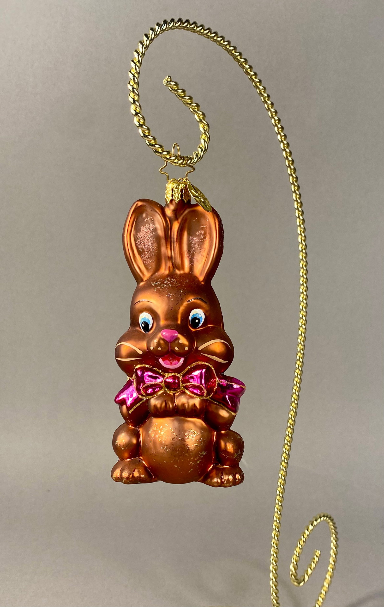 Christopher Radko Chocolate Bunny Glass Easter Ornament: A mouth-blown glass holiday ornament by Christopher Radko, designed in the form of a seated chocolate Easter bunny. The rabbit features an iridescent metallic bronze-brown finish to simulate molded ch