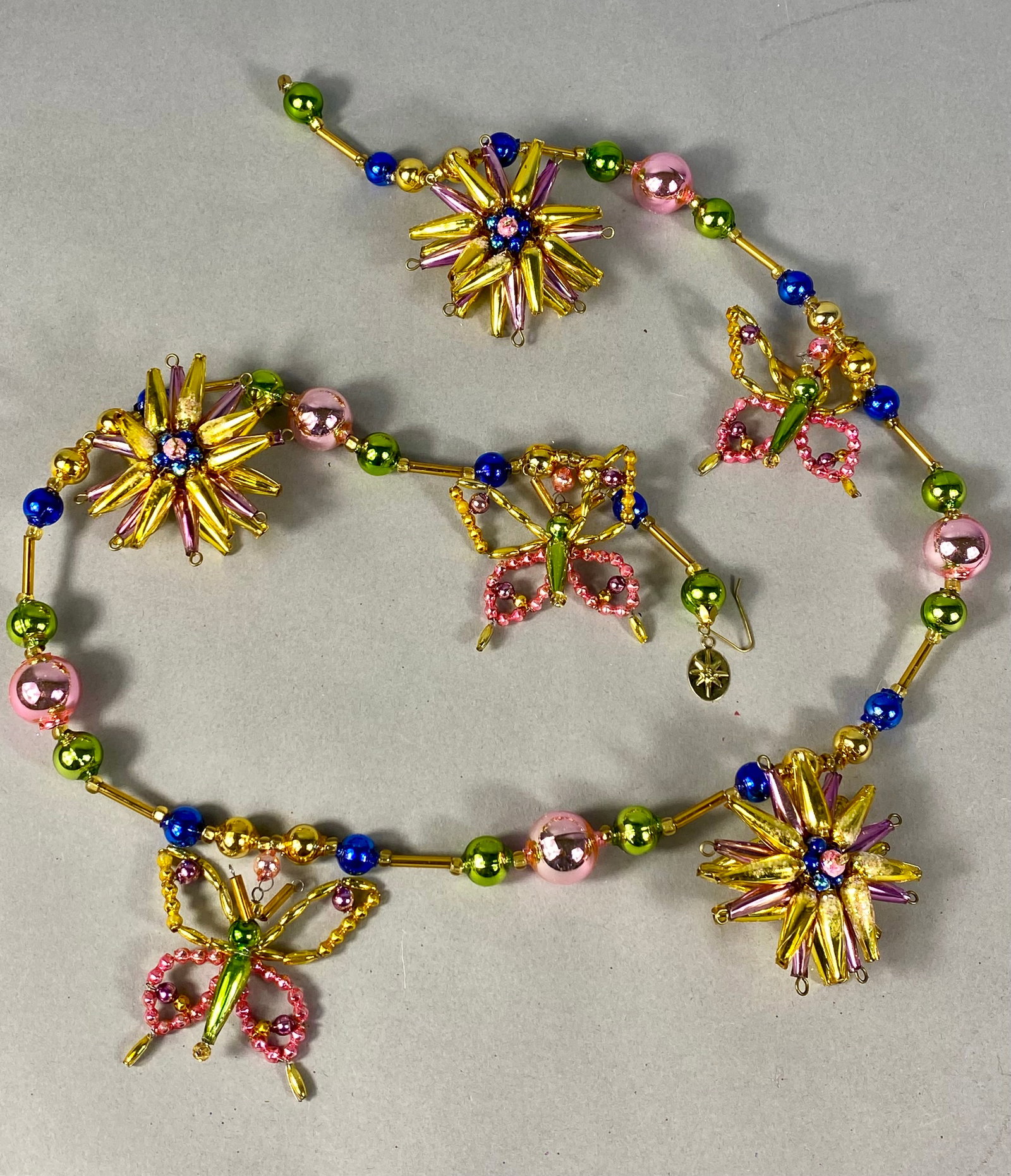 Christopher Radko Springburst Glass Beaded Butterfly and Starburst Garland: A decorative beaded garland attributed to Christopher Radko in the Springburst pattern. The piece is constructed on gold-tone metal wire and features a variety of multicolored glass beads. Design elem