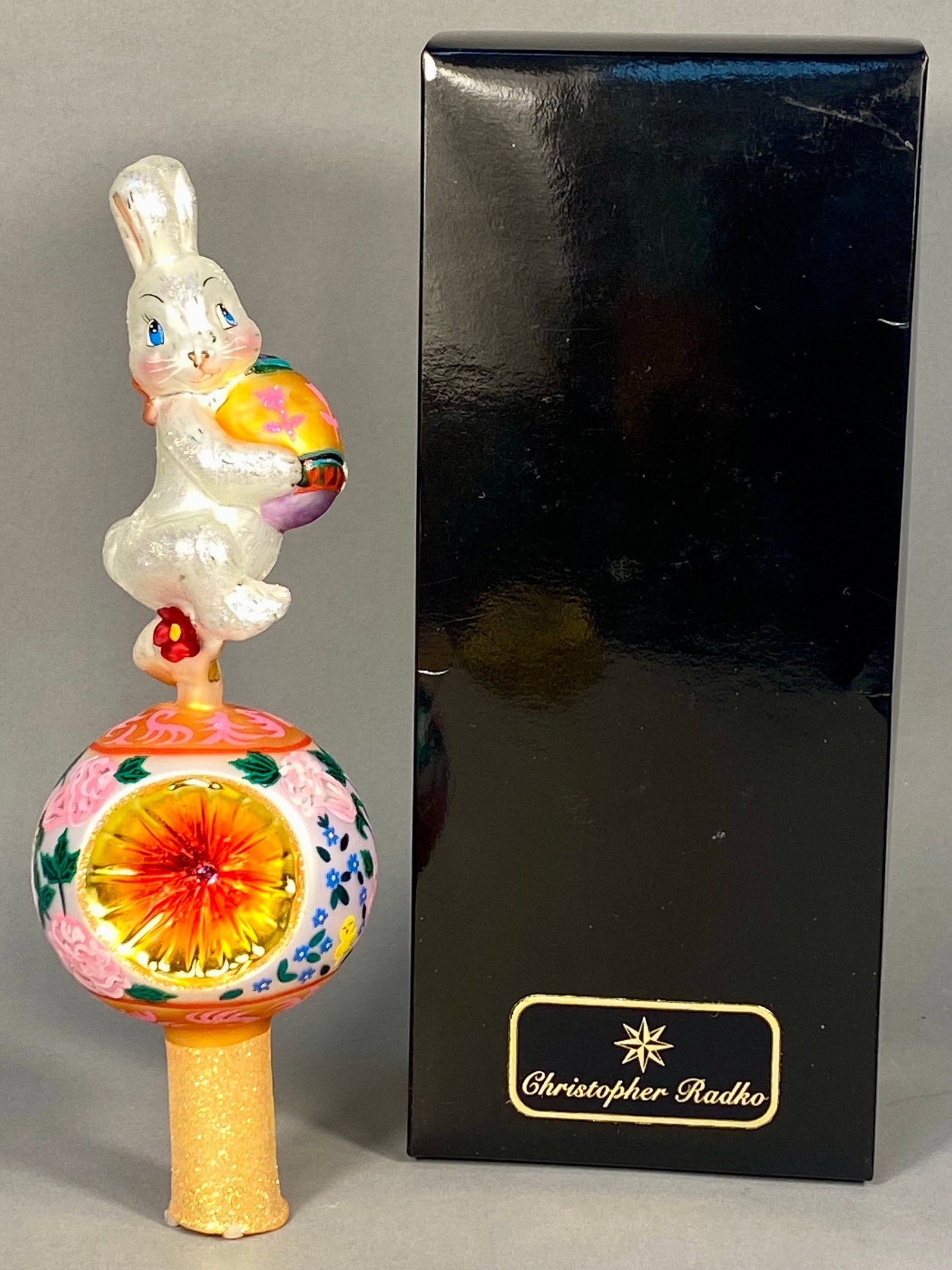 Christopher Radko A Hop on Top Hand Blown Glass Easter Tree Topper: This hand-blown glass tree topper is titled A Hop on Top by Christopher Radko, model number 00-188-0. The piece features a white Easter bunny figure with an iridescent glitter finish, blue eyes, and p