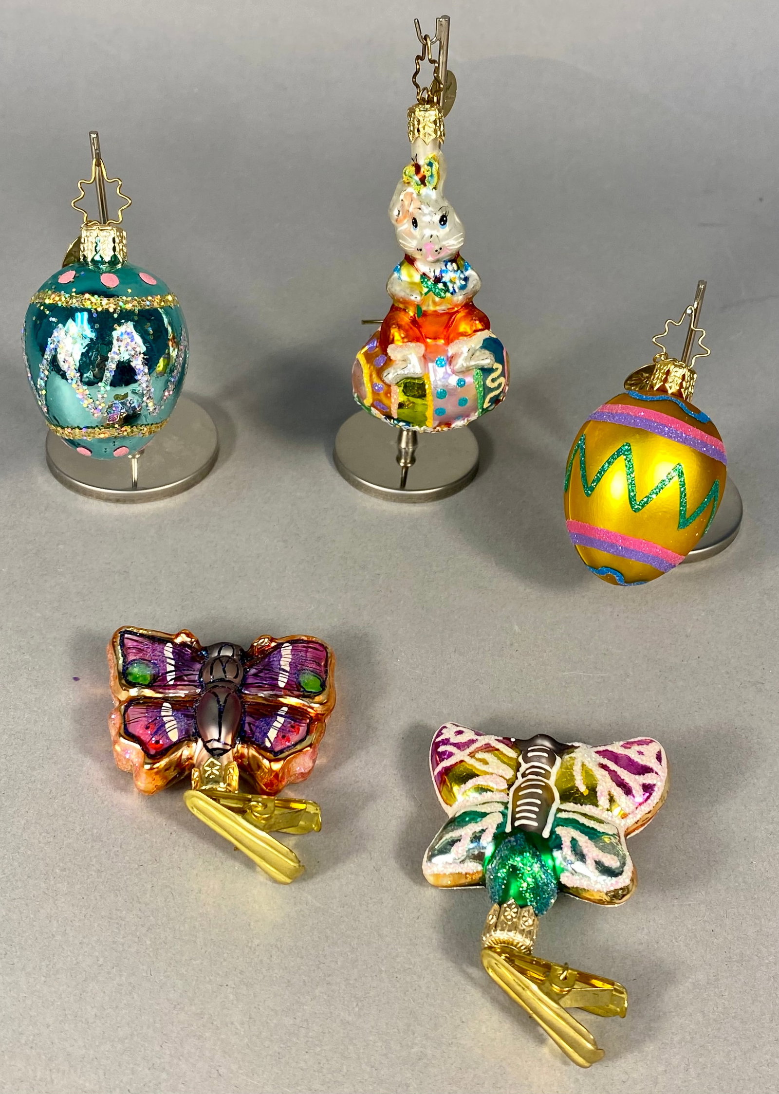 A Group of Five Christopher Radko Hand-Blown Glass Easter Ornaments: A group of five hand-blown glass holiday ornaments produced by Christopher Radko, featuring Easter and springtime themes. The lot includes a figural rabbit perched on a decorated egg, two individual e