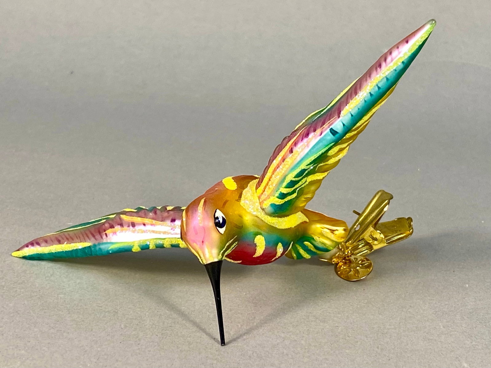 Christopher Radko Holiday Hummer Glass Hummingbird Clip-On Ornament: This hand-blown glass Christmas ornament is the Holiday Hummer pattern by Christopher Radko. The piece is shaped as a hummingbird in flight and features a vibrant polychrome color palette including pi