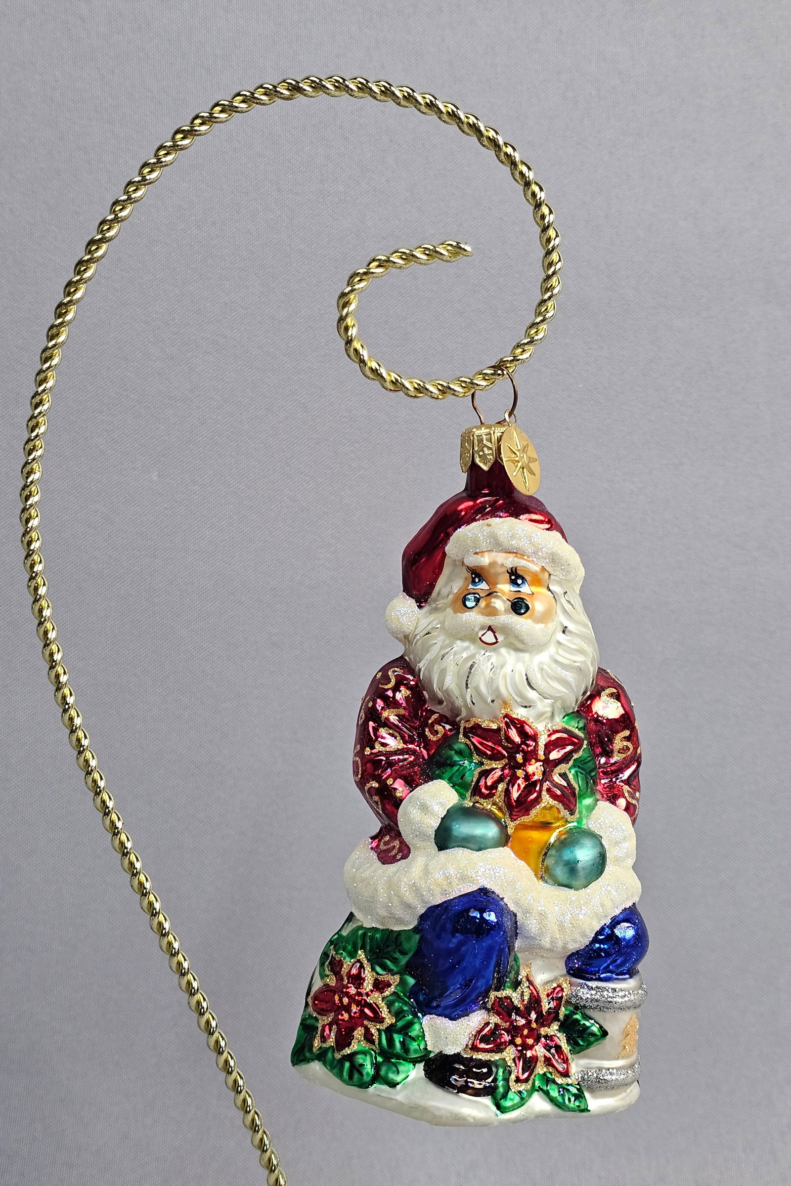 Christopher Radko Hand-Blown Glass Santa Claus with Poinsettias Christmas Ornament: This is a hand-blown glass Christmas ornament produced by Christopher Radko, featuring a traditional Santa Claus figure. The ornament is mouth-blown into a mold, silvered internally for brilliance, an