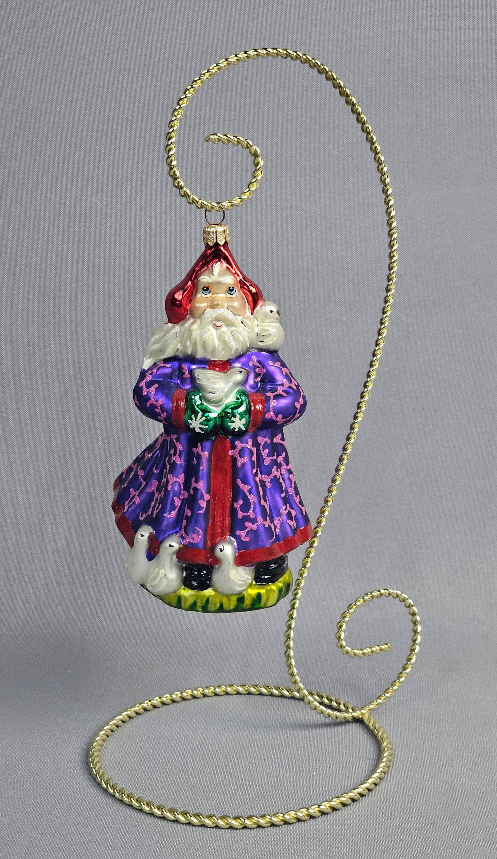 Polish Mouth-Blown Glass Father Christmas Ornament with Birds: A handcrafted Polish mouth-blown glass Christmas ornament depicting a Father Christmas figure. The figure is dressed in a royal purple robe featuring elaborate pink glitter scrollwork and a central re