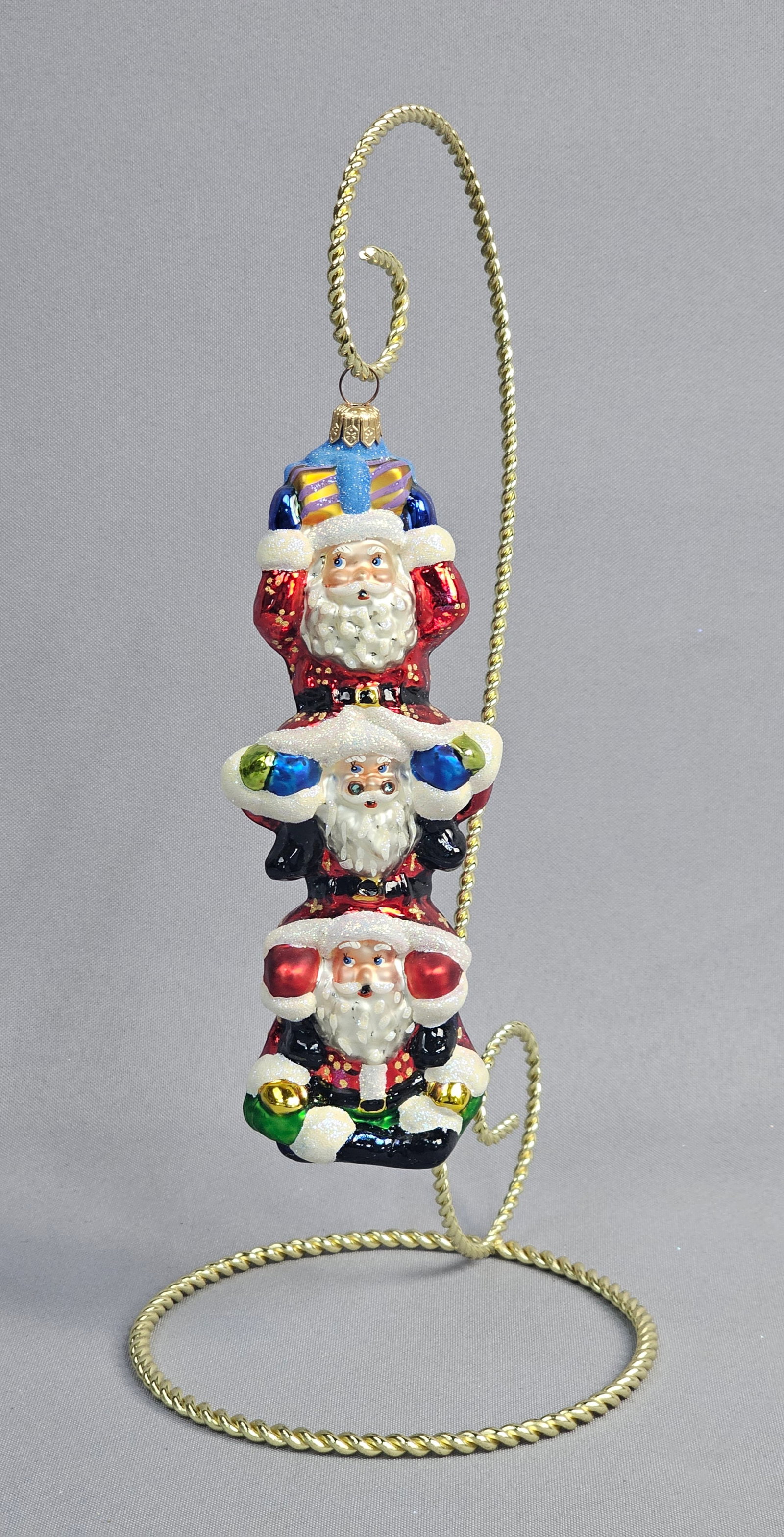 Christopher Radko Hand-Blown Glass Triple Stack Santa Christmas Ornament: This hand-blown glass Christmas ornament is produced by Christopher Radko and features a vertical stack of three festive Santas in graduated sizes. The top Santa is depicted in a metallic red suit wit