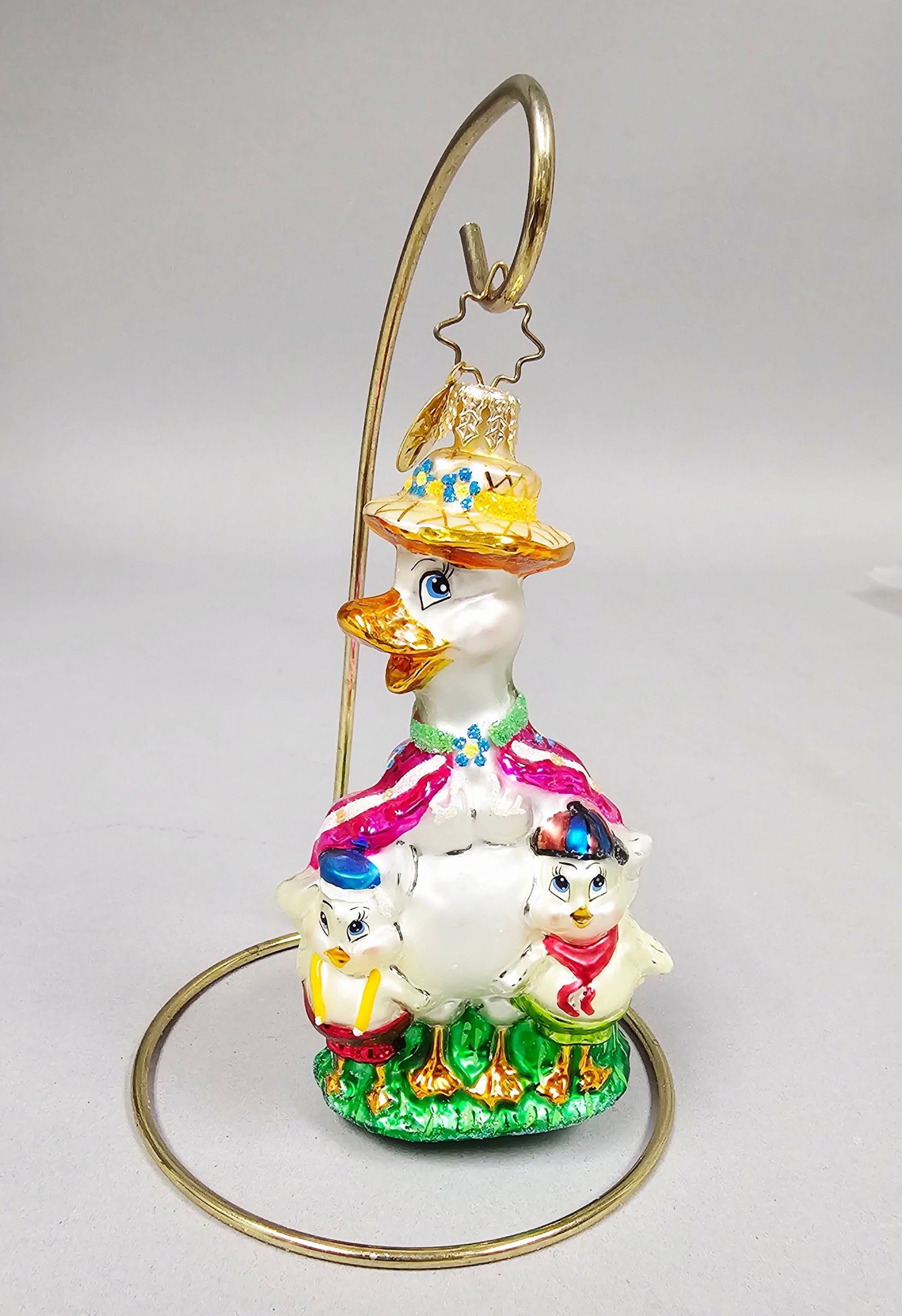 Radko Take a Gander Mother Goose Glass Ornament: Christopher Radko Take a Gander hand-painted, blown-glass figural ornament. The piece depicts Mother Goose wearing a yellow straw-style bonnet decorated with blue and yellow flowers, a green glittered
