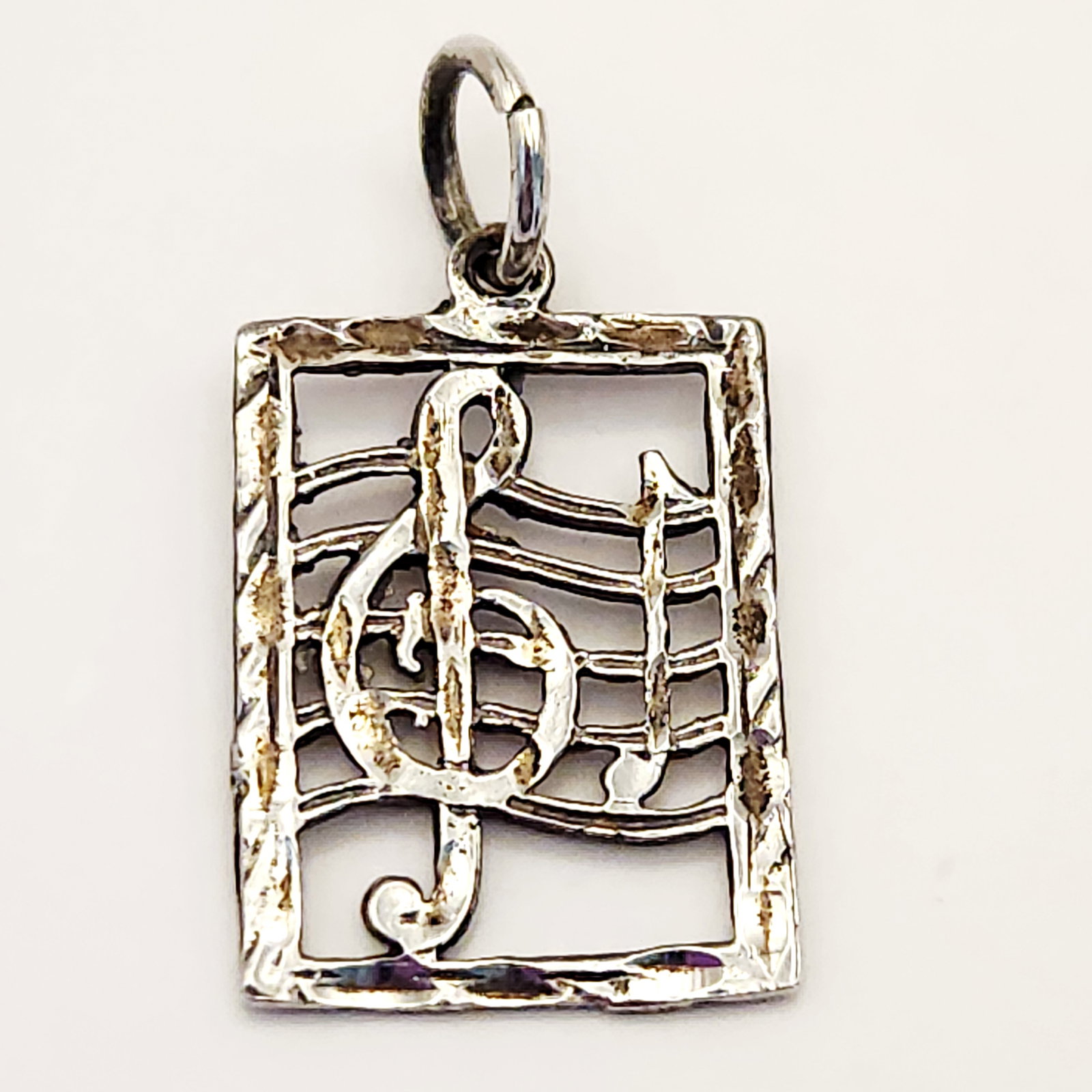 14K Treble Clef Pendant 1.7 Grams: This lot features a 14-karat white gold pendant designed with a musical theme. The openwork rectangular pendant contains a central motif of a treble clef (G-clef) placed over a four-line musical