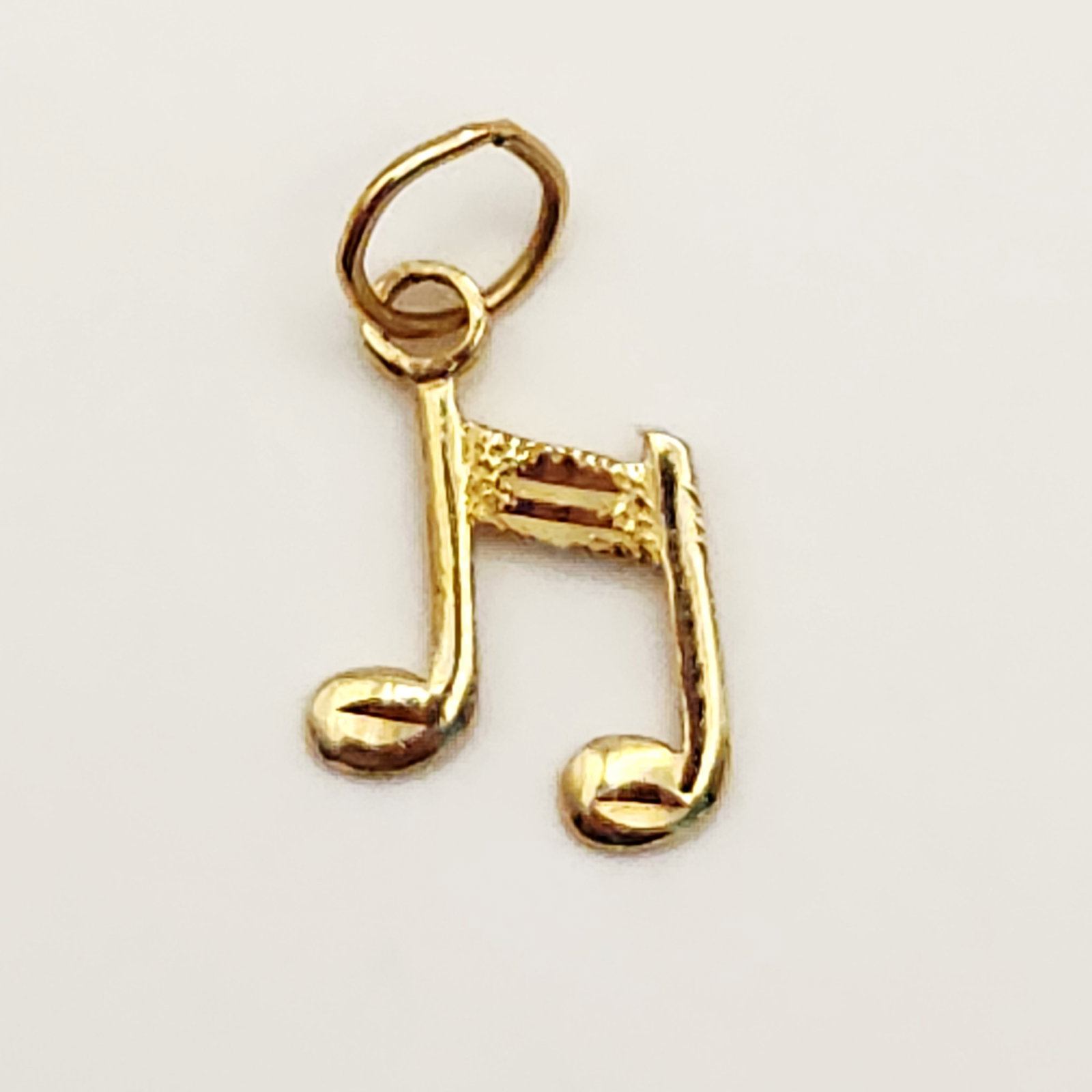 14K Musical Note Charm 0.4 Grams: A 14 karat yellow gold charm designed as a beamed pair of eighth notes. Dimensions: Approximately 0.5 inches in total length Weight: Approximately 0.4 grams. The gold charm appears to be in good