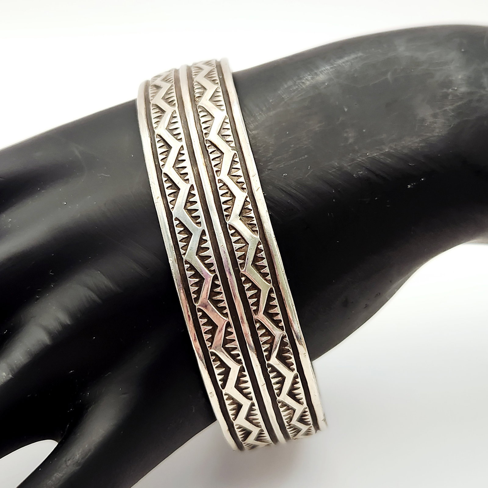Sterling Navajo Cuff Bracelet 60.1 Grams: This sterling cuff bracelet features a deeply stamped geometric pattern across its exterior surface. A single maker mark consisting of a stylized capital letter A with a horizontal bar across the