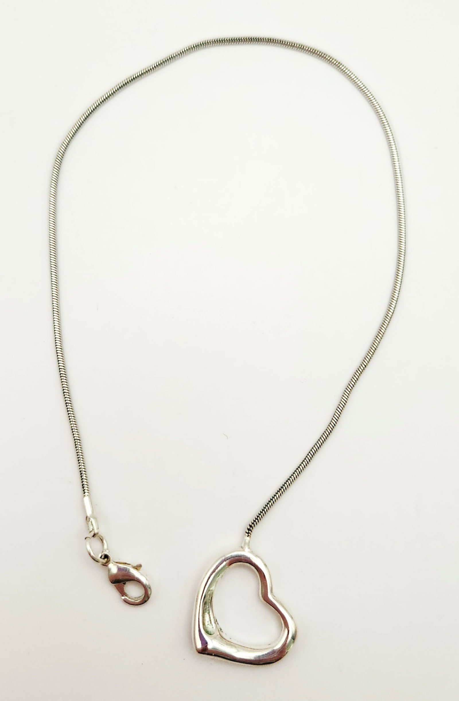 Tiffany Elsa Peretti Sterling Heart Chain 6.2 Grams: This sterling silver chain features an asymmetric open-heart pendant from the Tiffany & Co. Elsa Peretti collection. The pendant is suspended from a sterling silver snake chain that fastens with a