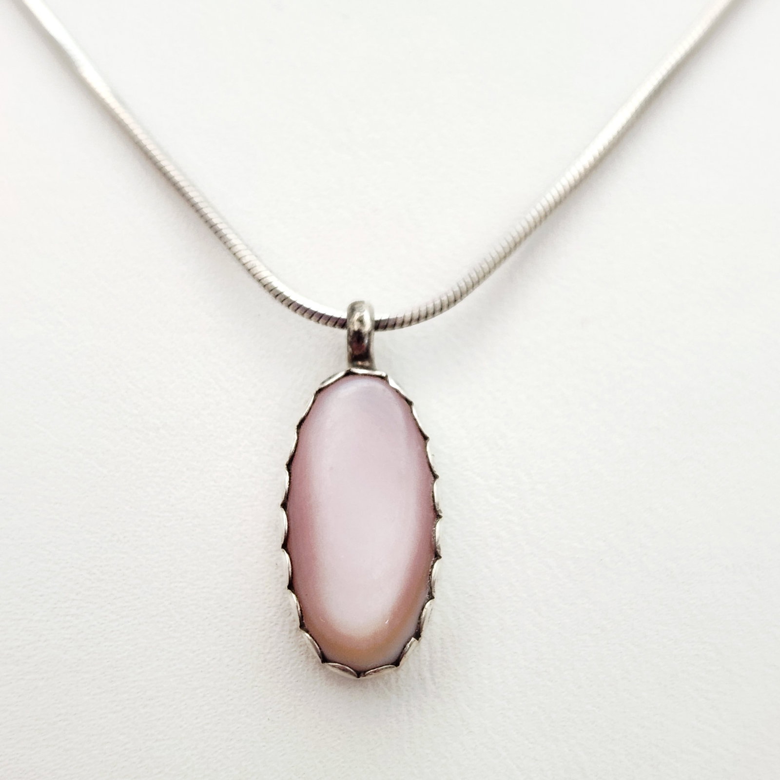 Charlotte Begay Sterling Necklace 4.9 Grams: This Navajo sterling silver necklace features an oval cabochon pendant of pink shell, possibly mother of pearl or conch shell, set within a scalloped sawtooth bezel. Length: 16 inches Weight: 4.9