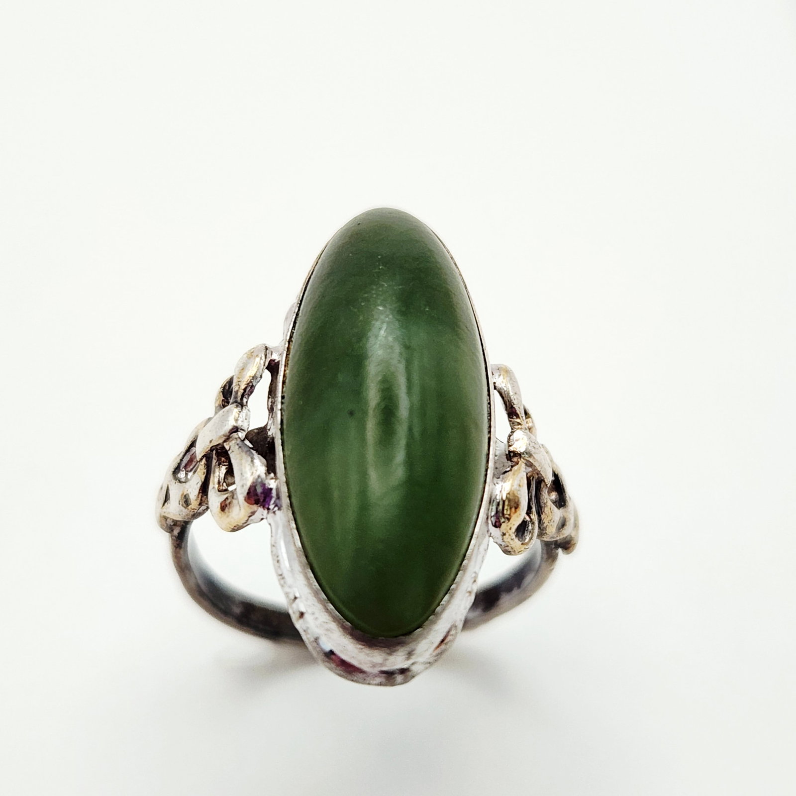 Sterling & 10K Gold Jade Ring 3.8 Grams: A sterling silver and 10K gold ring featuring an oval green jade cabochon and decorative bow shoulders, weighing 3.8 grams and measuring US size 5.5. Good condition, some tarnishing.