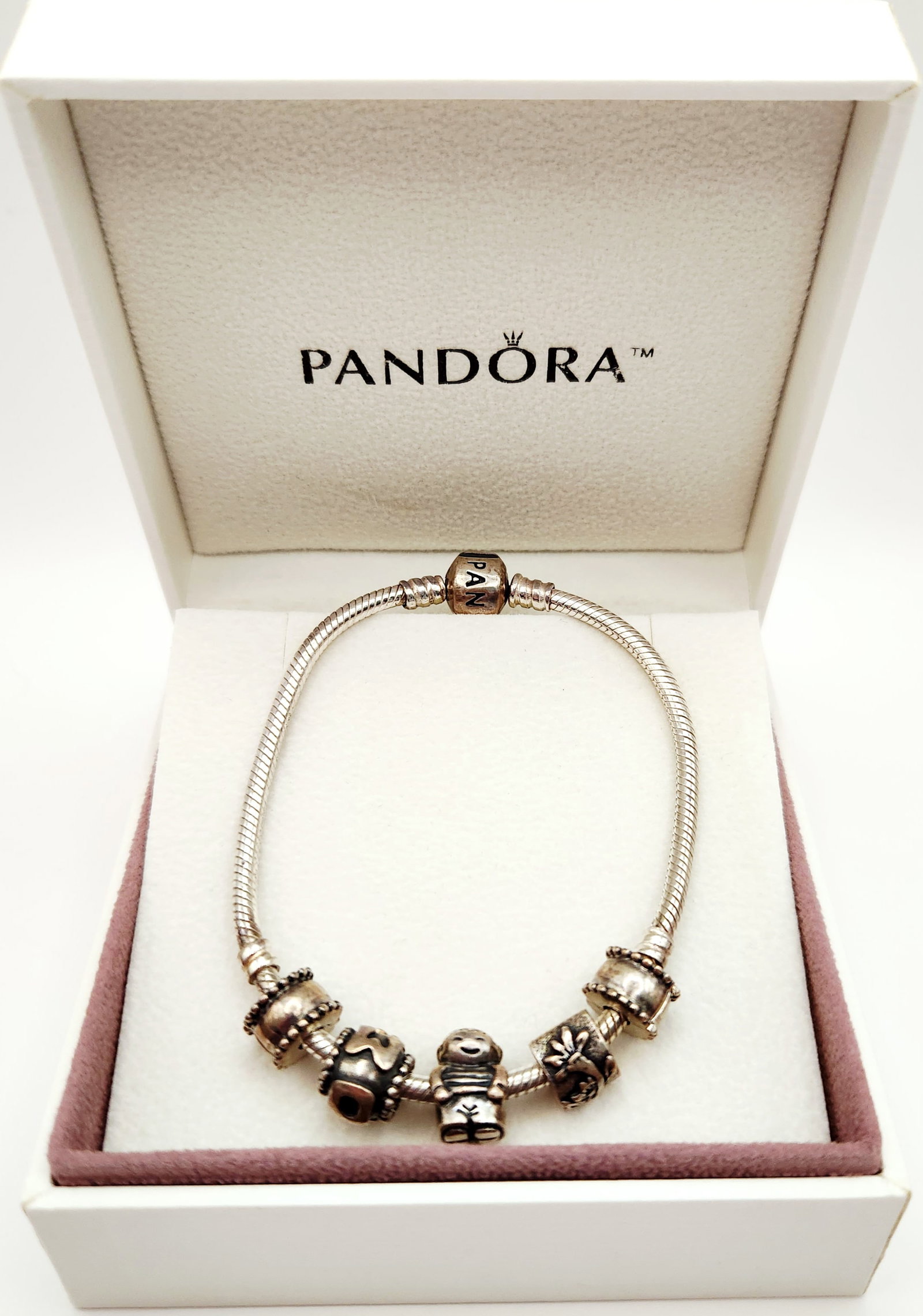 Pandora Sterling Charm Bracelet 29.8 Grams: A Pandora sterling silver snake chain charm bracelet featuring a barrel clasp. The bracelet is adorned with a collection of charms, including two beaded spacers, a bead with cutout heart-like motifs,