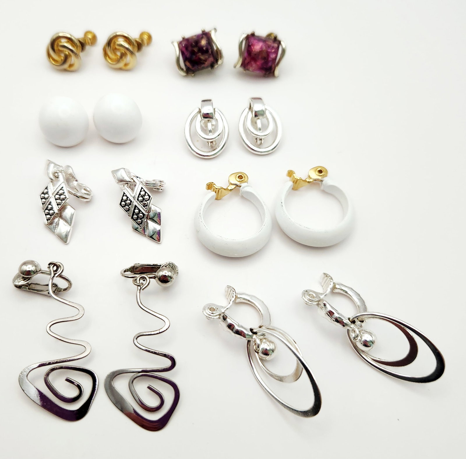 Signed Vintage Clip-on and Screw-back Earrings: A collection of vintage costume clip-on and screw-back earrings in gold-tone, silver-tone, white, and purple finishes featuring branded pieces ranging in length from 0.5 to 2.5 inches. Including, Mone