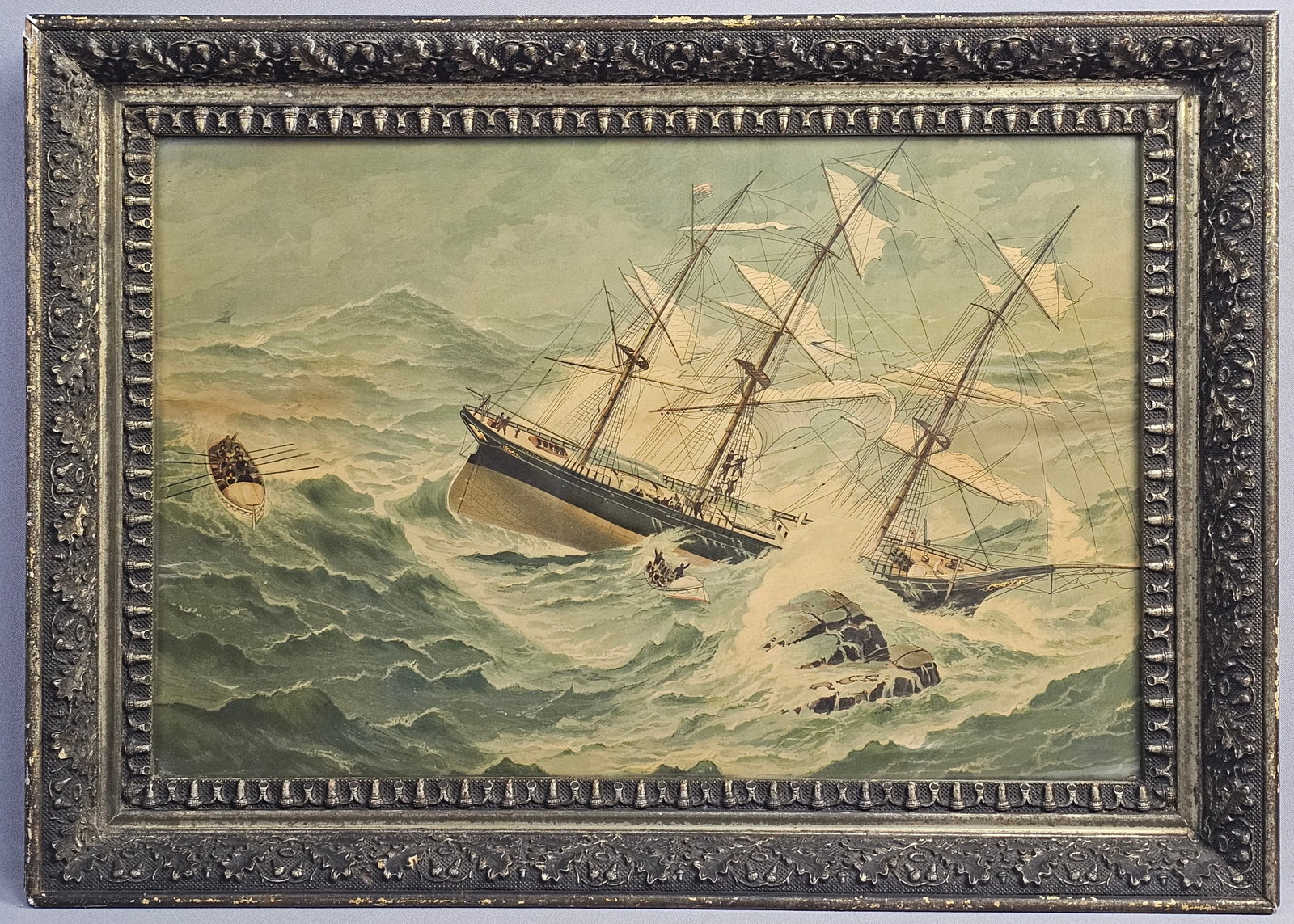 Framed 19th Century Maritime Lithograph of Shipwreck: The central subject is a three-masted clipper ship shown in distress among turbulent, high-crested waves near jagged rocky outcroppings. The scene includes two lifeboats; one is prominently featured