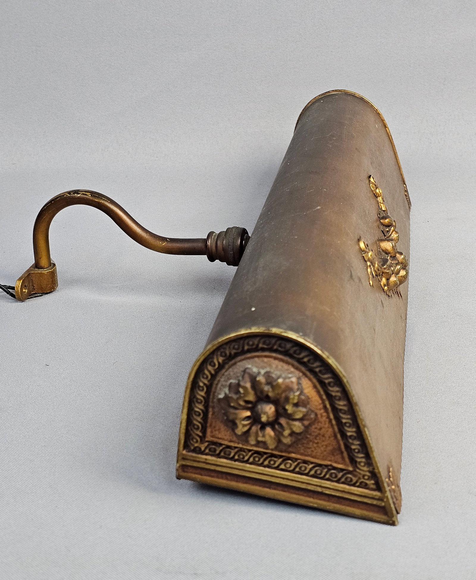 Vintage Antiqued Metal Wall Mounted Picture Light: This vintage wall-mounted picture light is designed in the Neoclassical style, featuring a rounded rectangular shade with applied cast-metal decorative elements. The exterior is finished in an