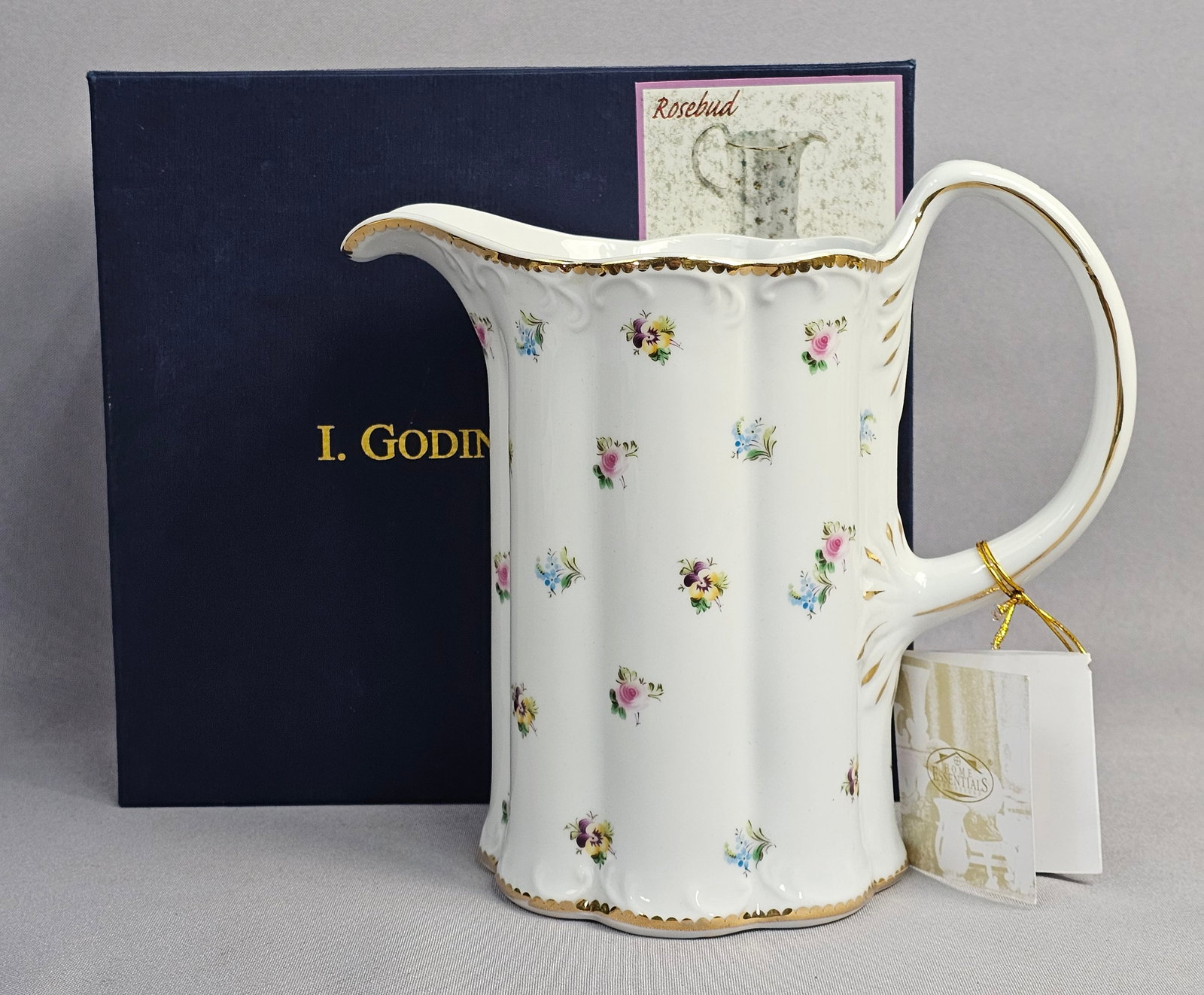 I. Godinger and Co. Rosebud Pattern Porcelain Pitcher: A white porcelain pitcher in the Rosebud pattern, manufactured for I. Godinger and Co. The pitcher features a vertically fluted or lobed body, a flared scalloped spout, and an ornate C-scroll handle.